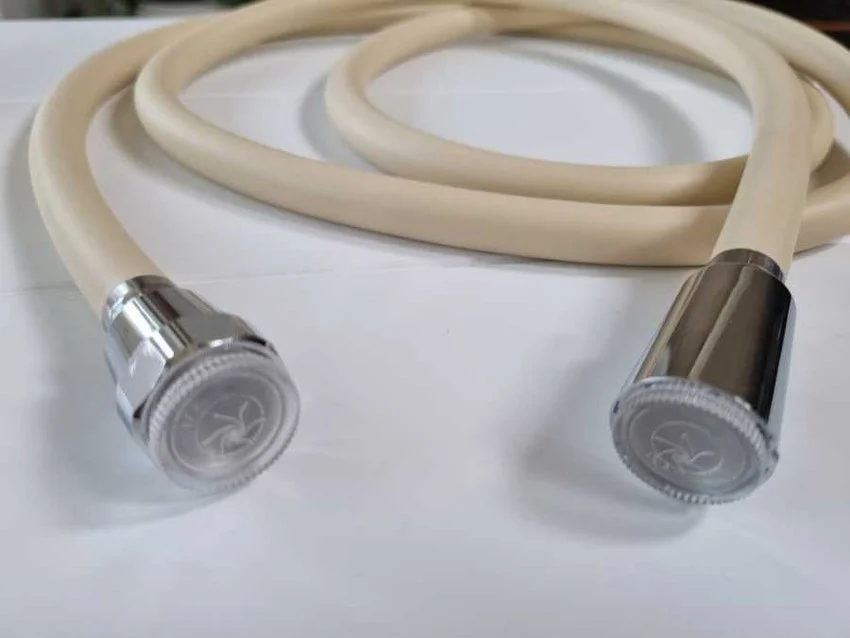 A beige rubber hose with metal fittings on both ends, laid out on a white surface.