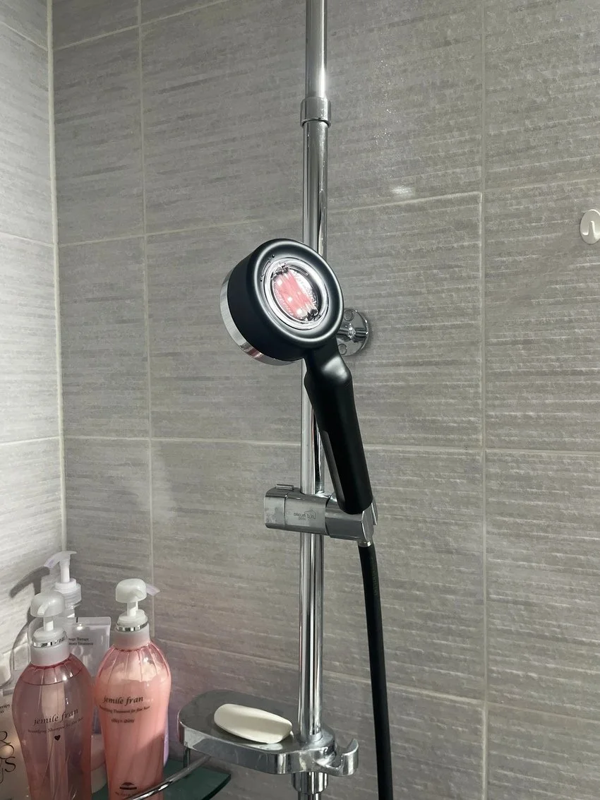 Showerhead mounted on a tiled wall with soap and pink lotion bottles on a shelf below.