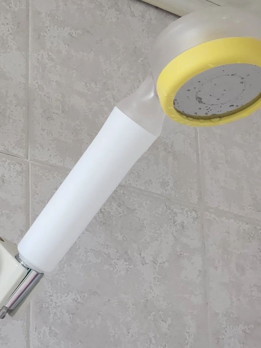 A water spray nozzle attached to a wall with a yellow and gray outlet, with a white paper towel wrapped around the nozzle.