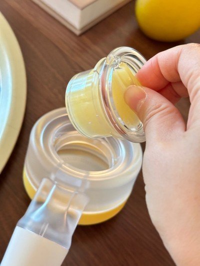 Close-up of a person opening a jar of yellow balm or cream with a spatula on a wooden surface.