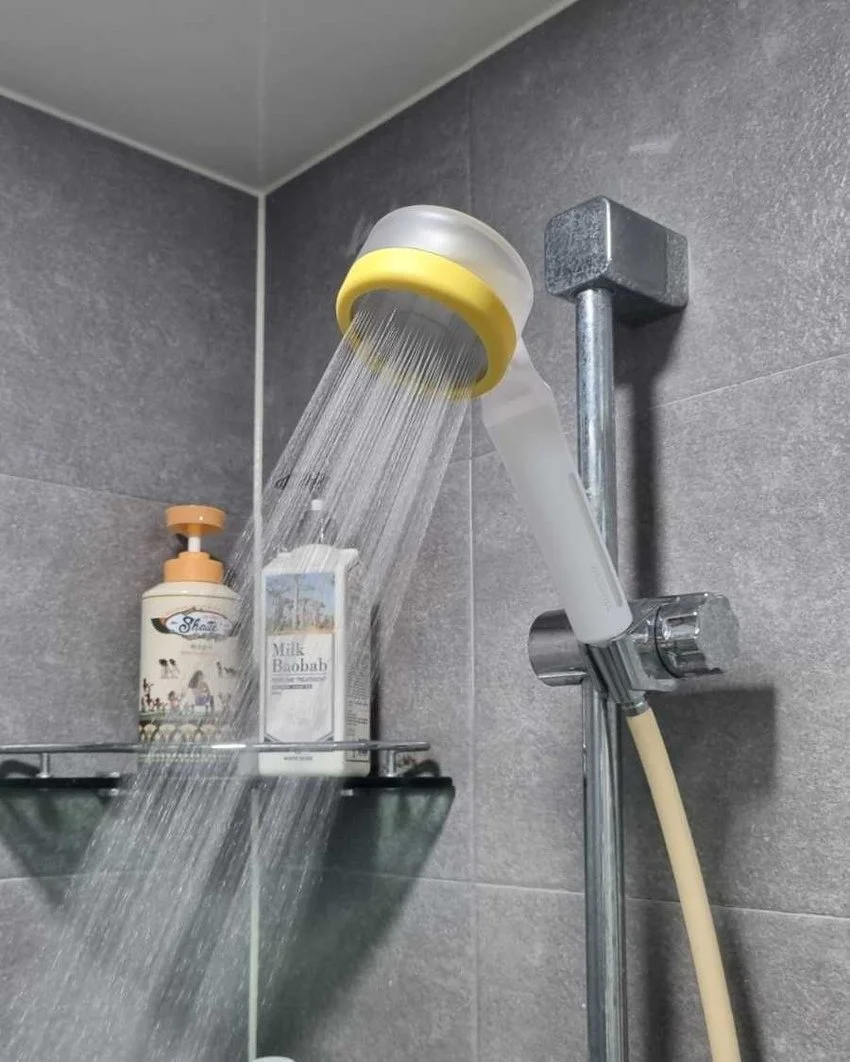 Shower with water running from the showerhead, soap dispenser, and a container of milk baileys on a metal shelf.