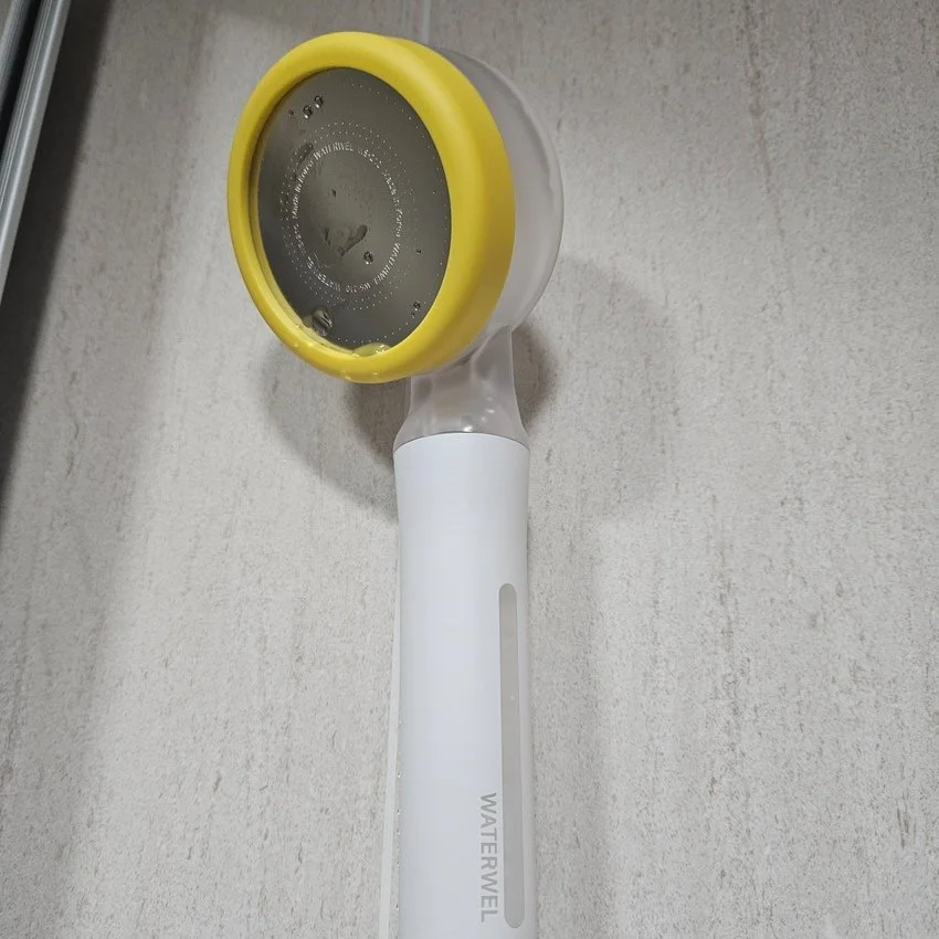 A White and yellow food chopper with a clear bowl, filled with water, sitting on a light beige surface.