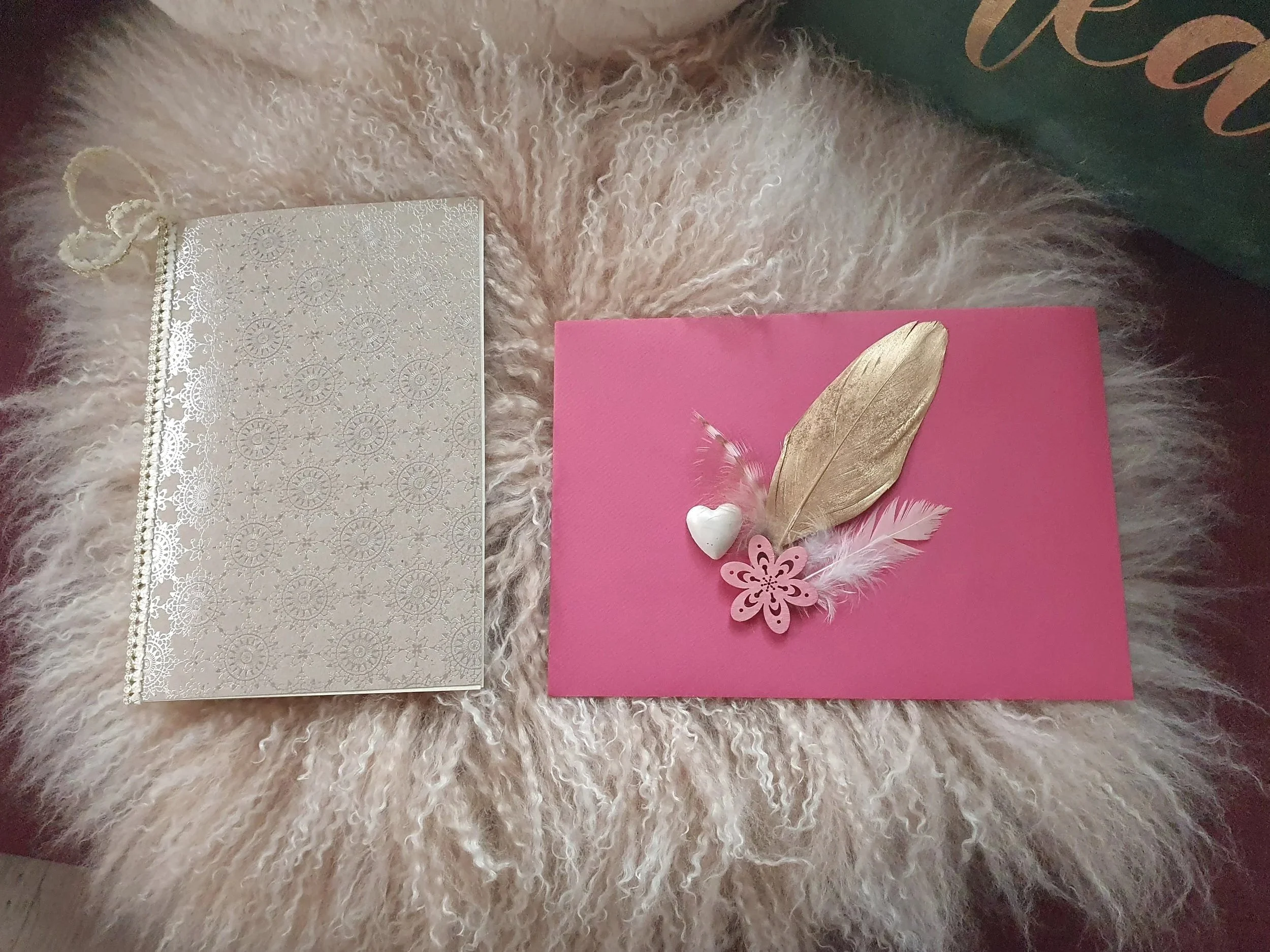 Eine Karte mit silbernem Muster, rosa Karte mit Goldfeder und Federn, kleinen Herz- und butterfly-Schmuckstücke, auf einem hellen, flauschigen Teppich