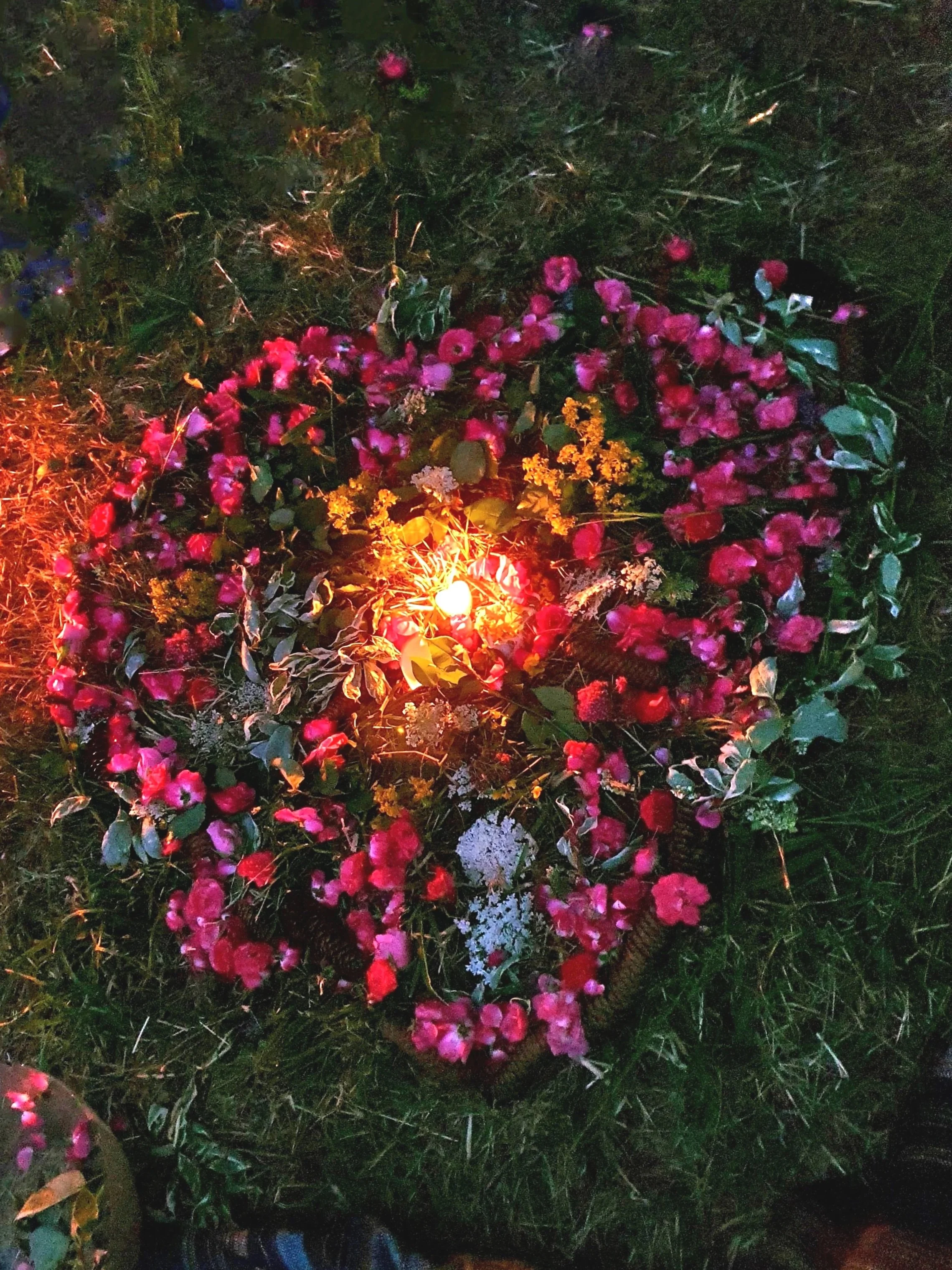 Blumen auf einem Grab, beleuchtet von Kerzenlicht bei Nacht.