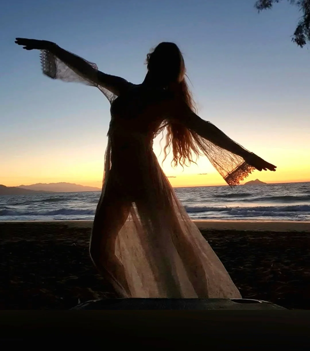 Eine silhouettierte Frau tanzt am Strand während des Sonnenuntergangs, mit dem Meer im Hintergrund.