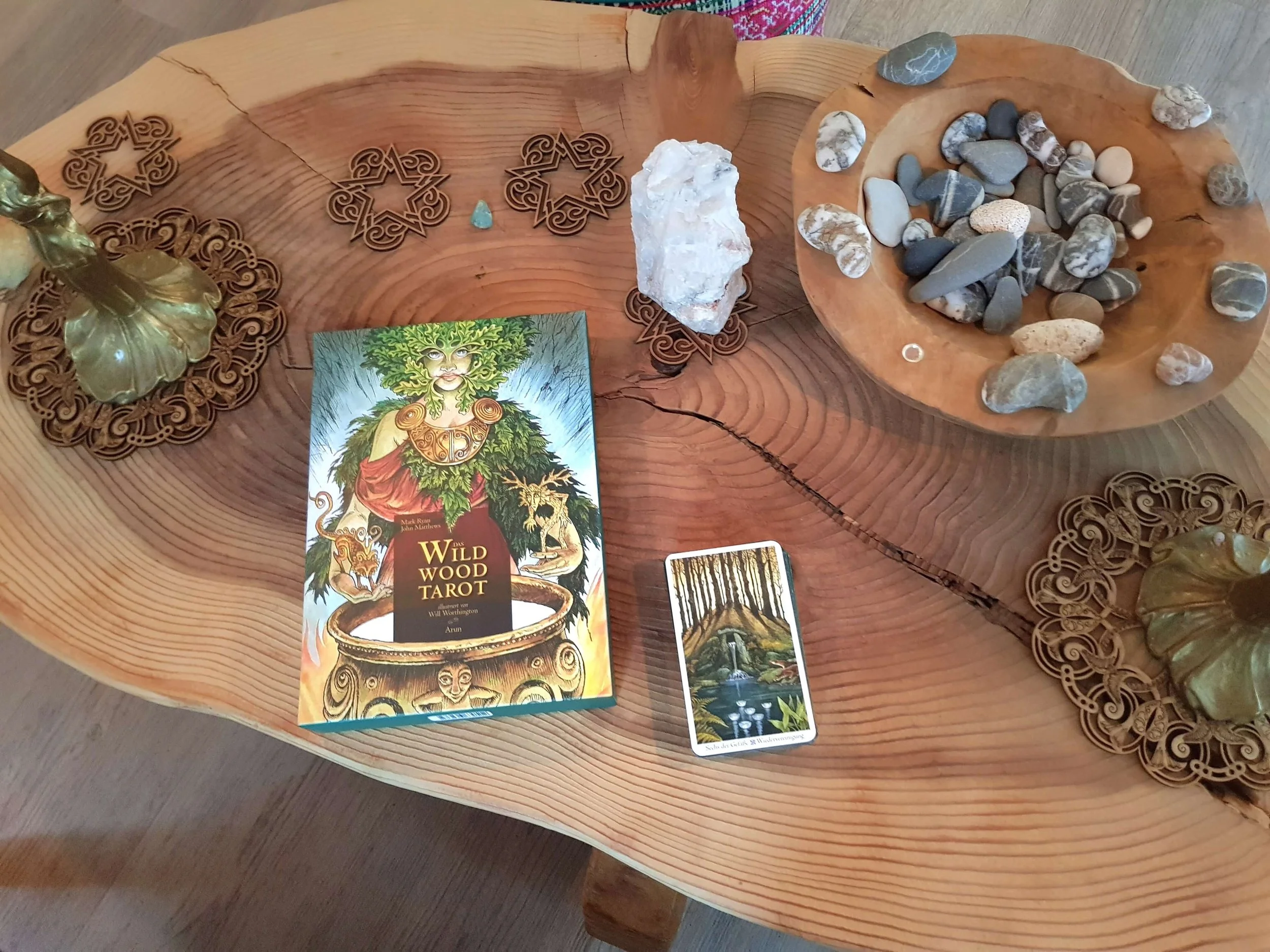 Ein Holztablett mit Steinen, einem Tarot-Kartensatz, einer Tarot-Postkarte, Holzdekorstücken und einer Karte mit einem Waldsee.