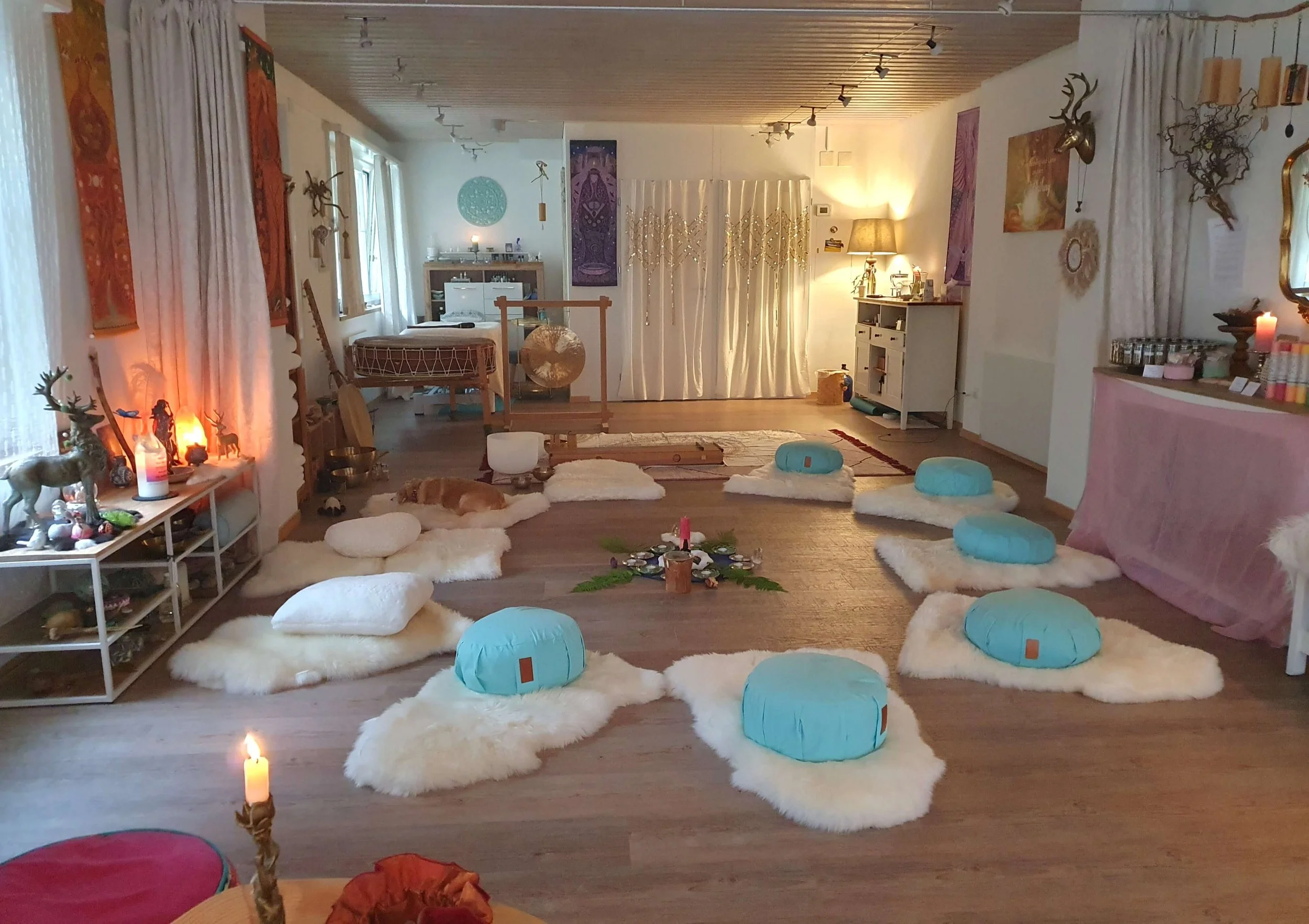 Gemütlicher Raum mit Kerzen, Polstern, Teppichen und Dekorationen im Skandinavischen Stil, wahrscheinlich für eine Zusammenkunft oder Meditation vorbereitet.