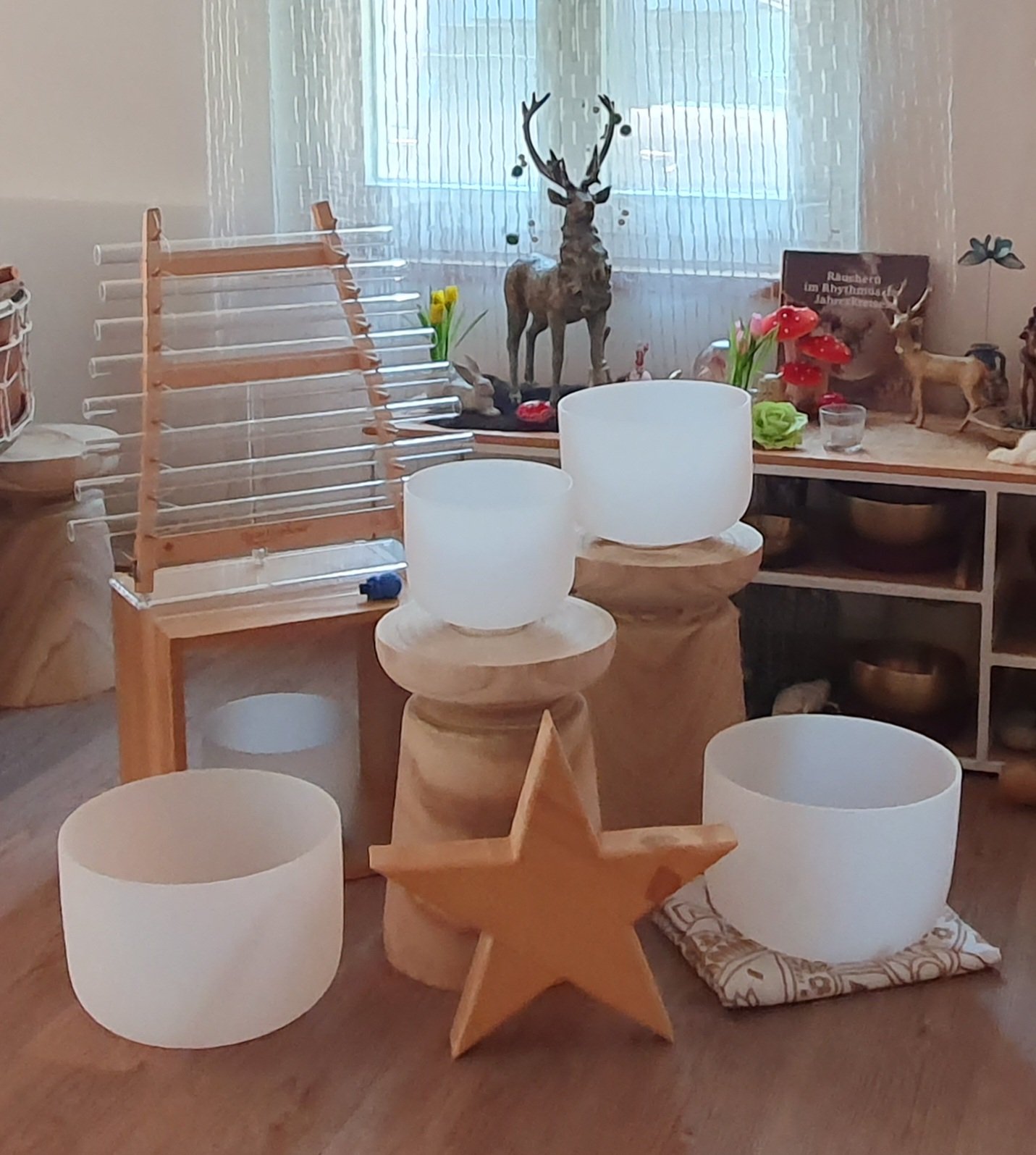 Ein gemütliches Raum mit Kerzenschein, Klangschalen, einem gongen, Holzstühlen und spirituellen Dekorationen, warmes Licht und große Fenster naturverbunden.
