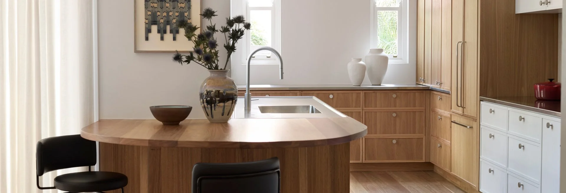 Modern kitchen with wooden cabinetry, white drawers, and a central island with a round edge, decorated with vases and a flower arrangement.