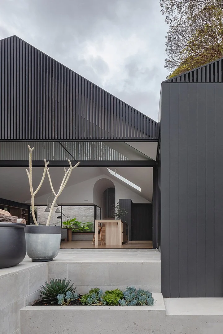 Modern house with black vertical siding, open interior with outdoor seating, potted plants, and succulent garden in a contemporary residential setting.