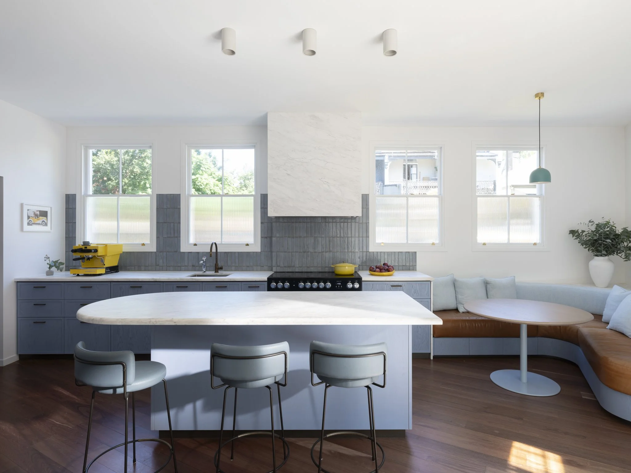 Modern kitchen with white cabinets, marble island, pendant light, and large windows showing greenery outside.