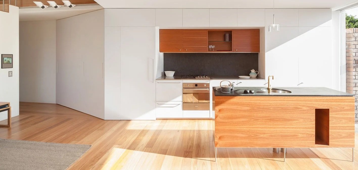Modern kitchen with wooden cabinets, black backsplash, white walls, and a kitchen island with a sink and gray countertop.