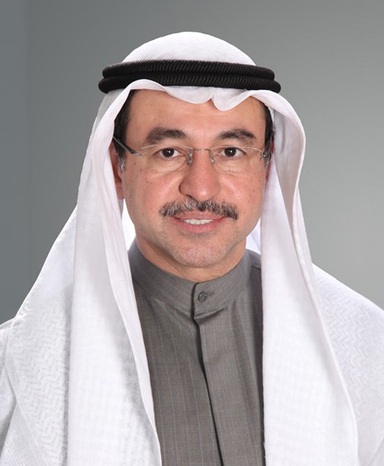 A man wearing traditional Middle Eastern attire, including a white headscarf with a black band and a gray thobe, smiling at the camera.