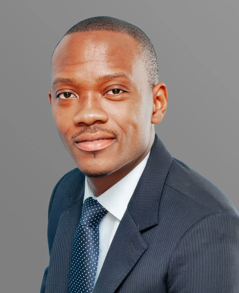 A portrait of a young man in a dark suit, white shirt, and dotted tie, smiling slightly against a plain gray background.