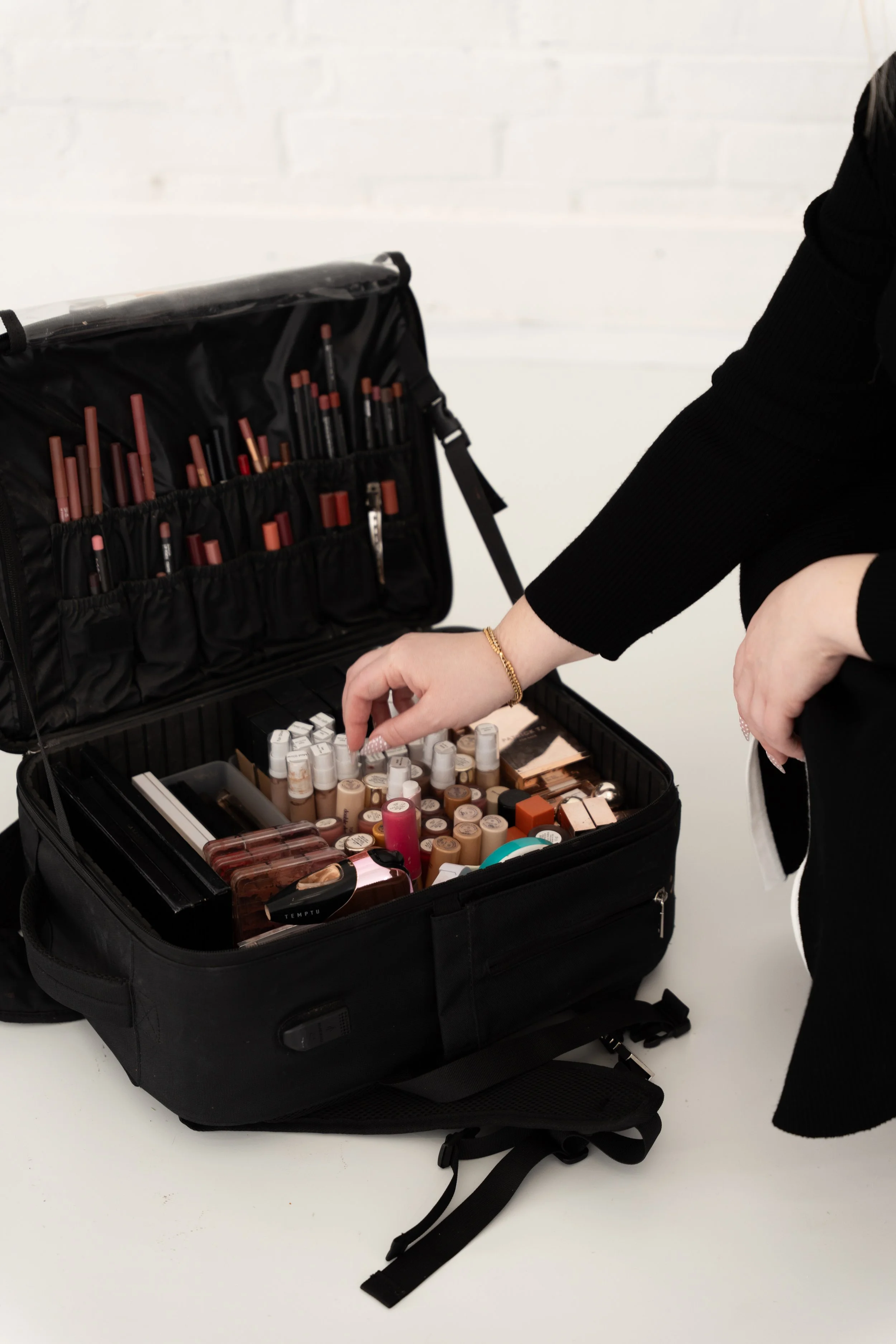 A woman organizing makeup products in a black case, which contains lipsticks, brushes, and other beauty supplies.