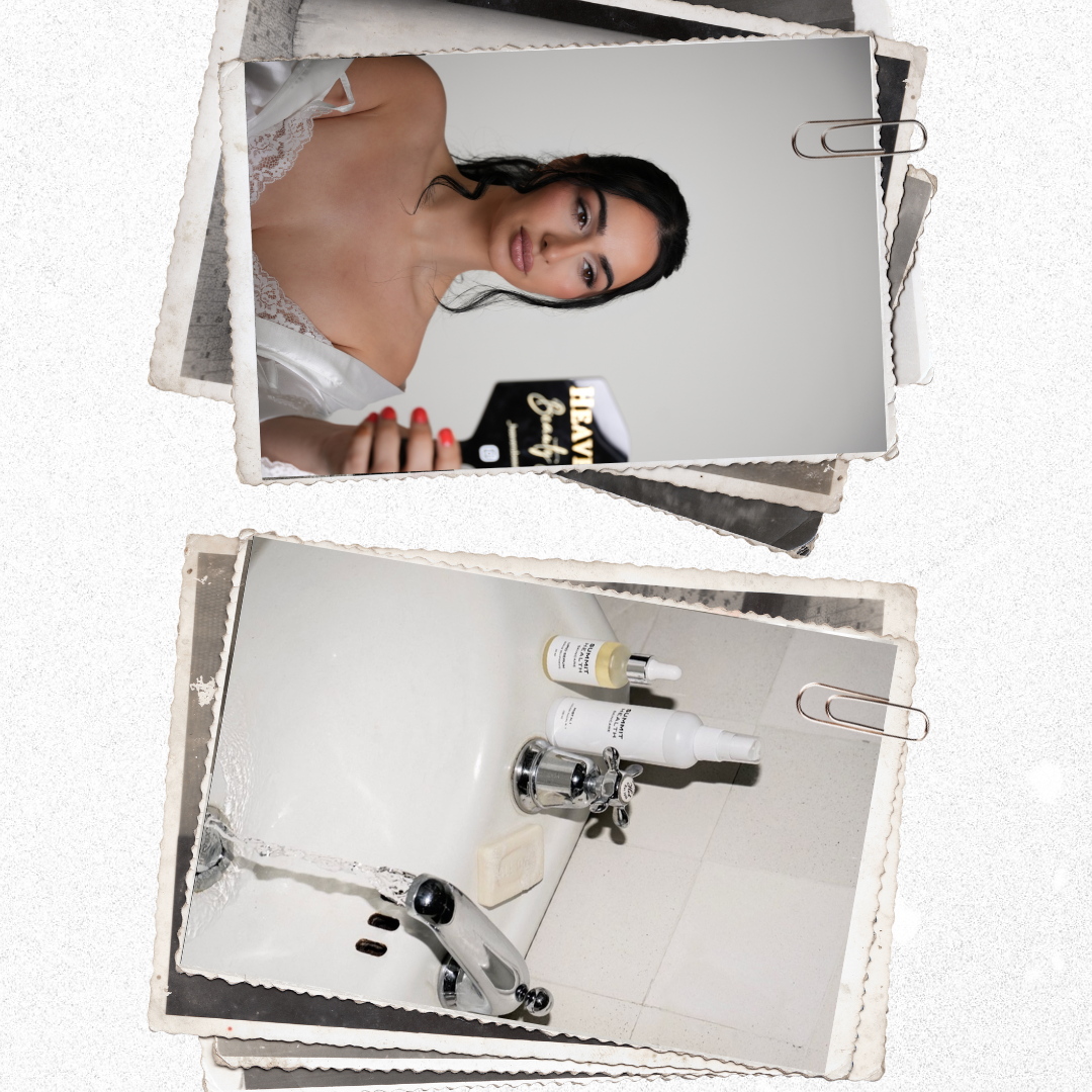 Photograph of a woman taking a selfie with her phone in a bathroom. The woman has long black hair and is wearing a white lacy top. The bathroom counter has bottles of skincare products and a bar of soap, with a silver faucet and running water.