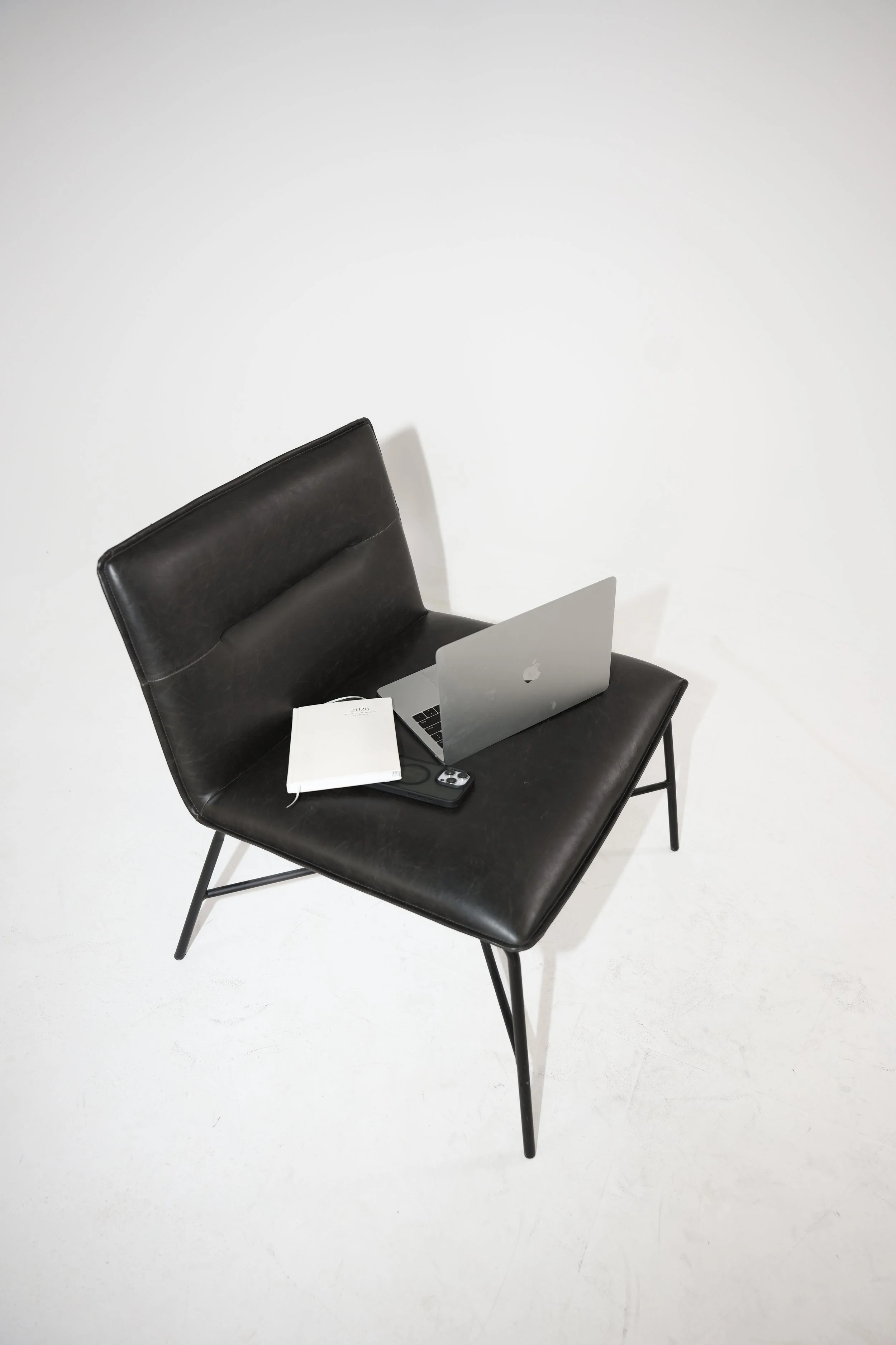 A black chair with a laptop, a notebook, and a smartphone on it, against a white background.