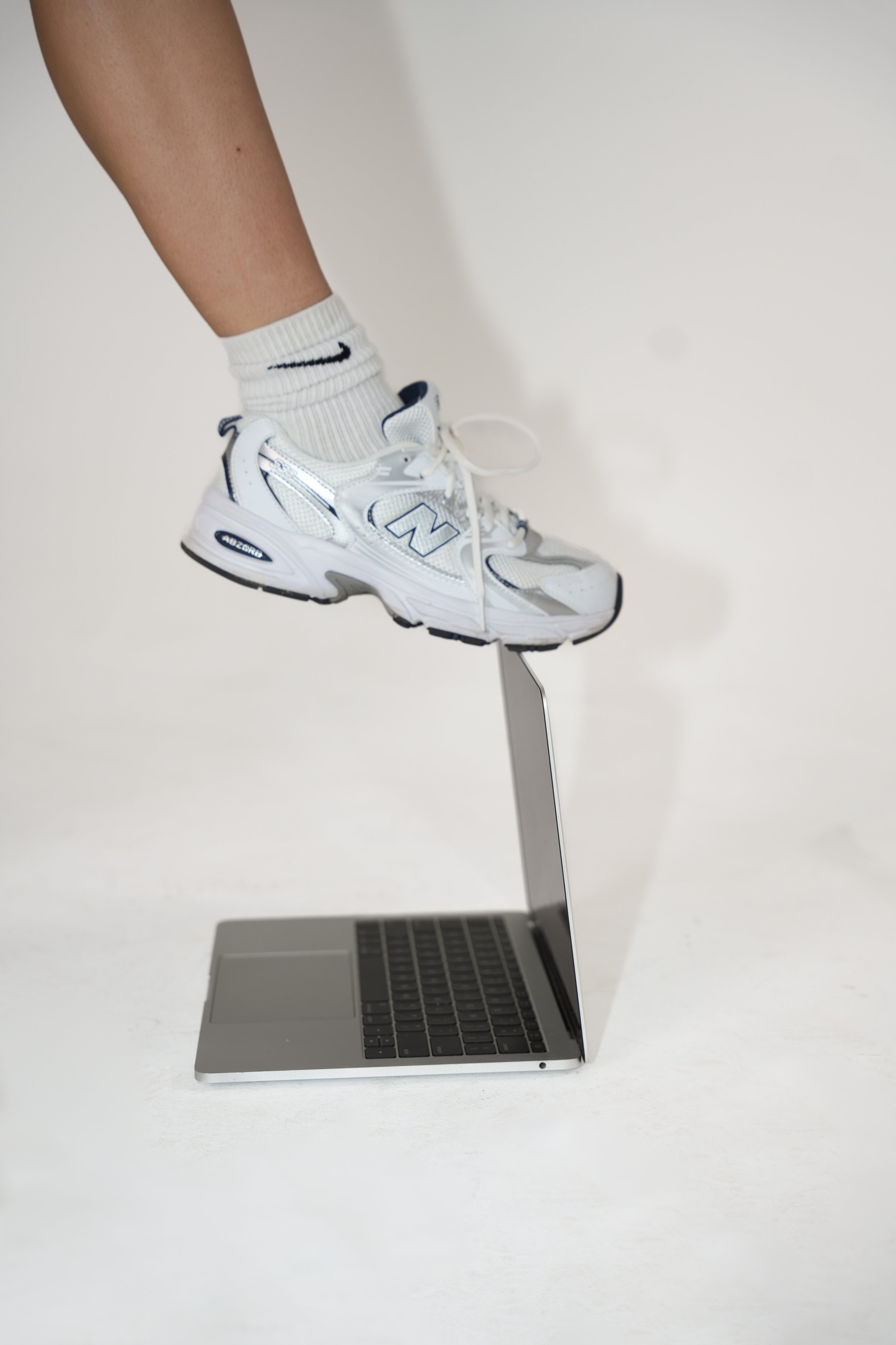 Person's foot in a white athletic shoe stepping on a laptop keyboard, with the laptop lid open.