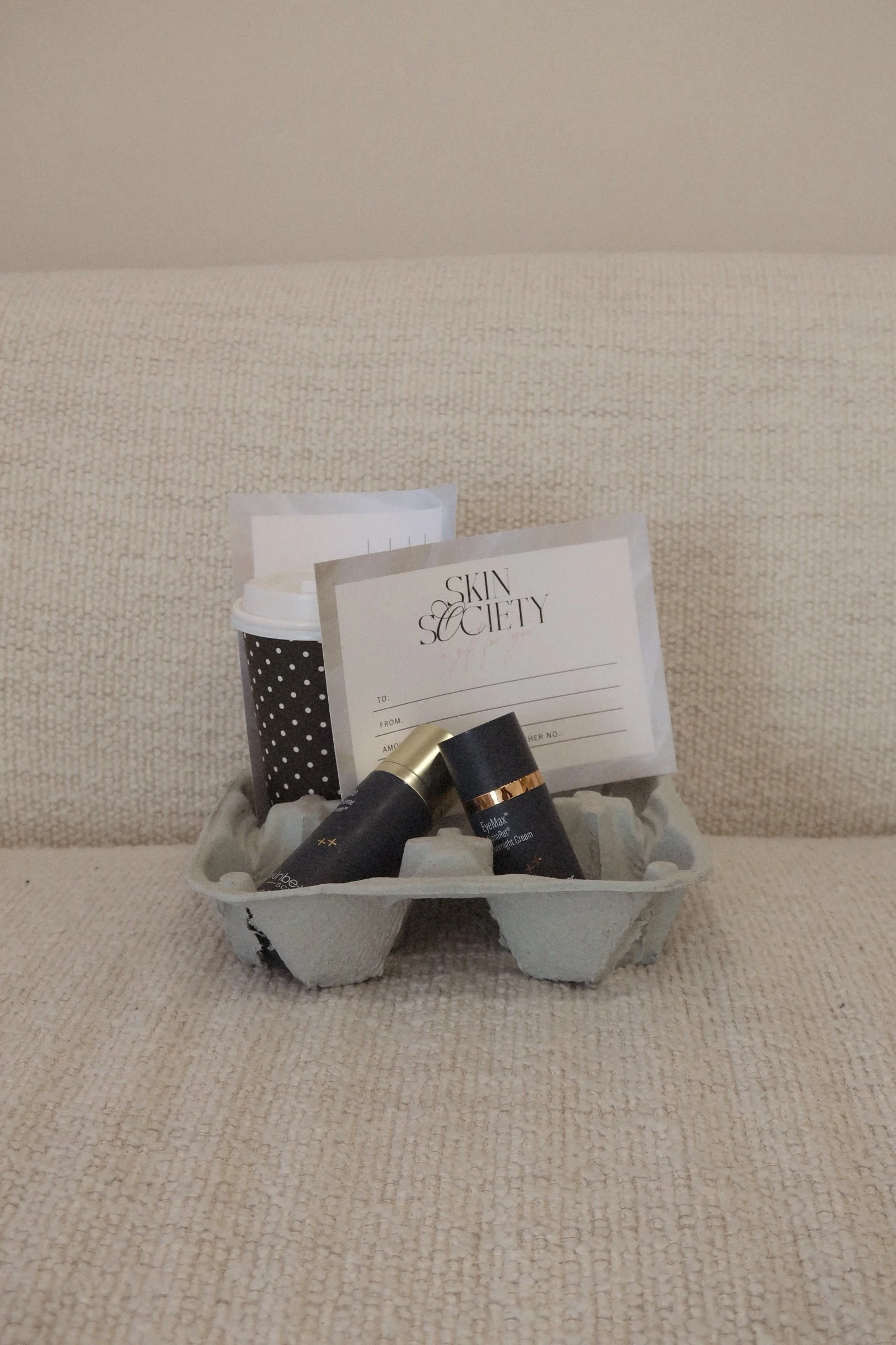 A gift basket containing skincare products and a Skin Society gift card on a beige textured surface.