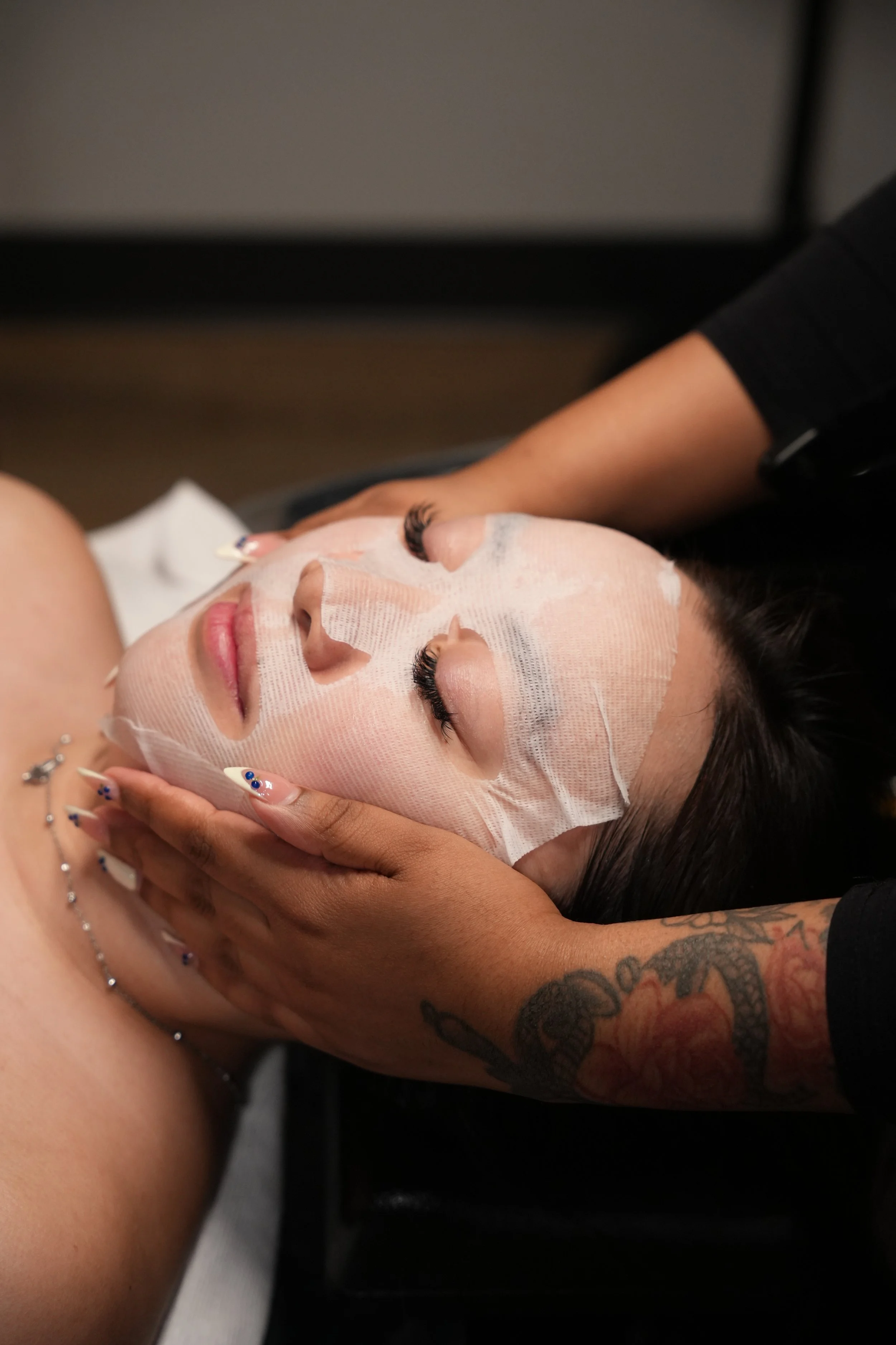 A woman receiving a facial treatment with a sheet mask at a spa or skincare clinic.