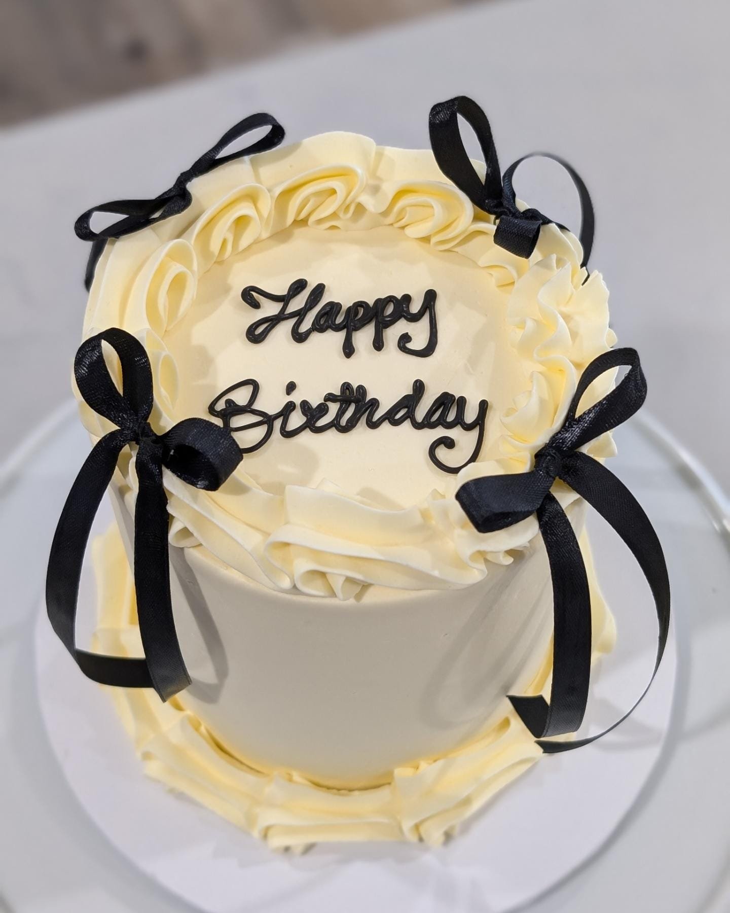 A white birthday cake decorated with black ribbons, white frosting, and a black script reading "Happy Birthday" on top.
