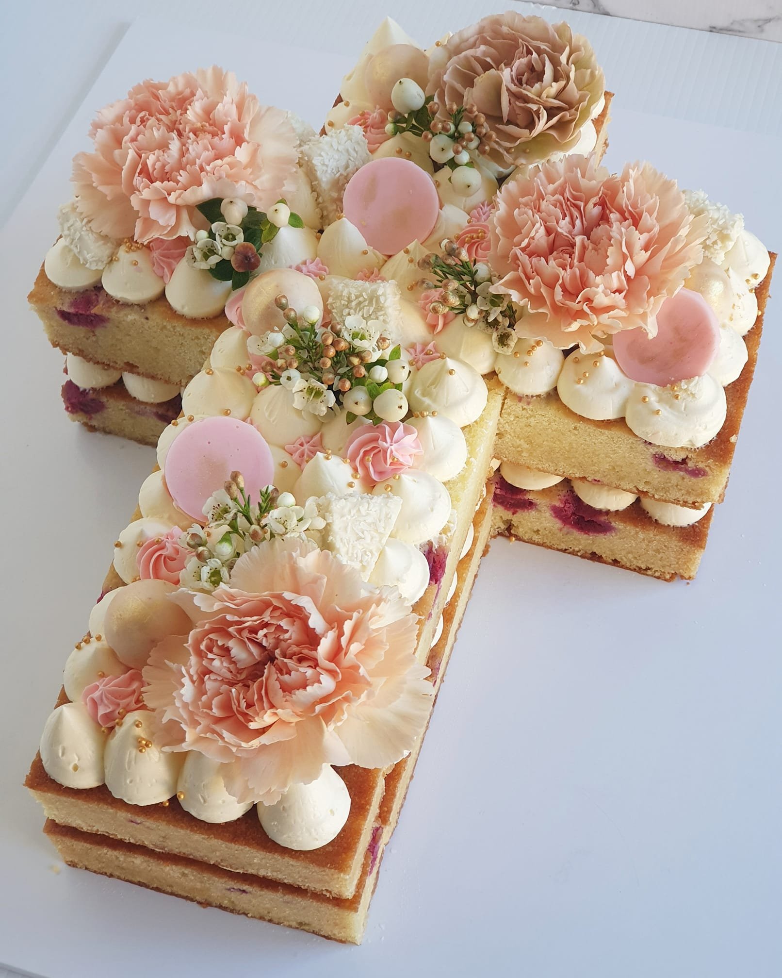 A cake decorated with pink carnations, white and pink flowers, cream dollops, and pink and white decorative elements.