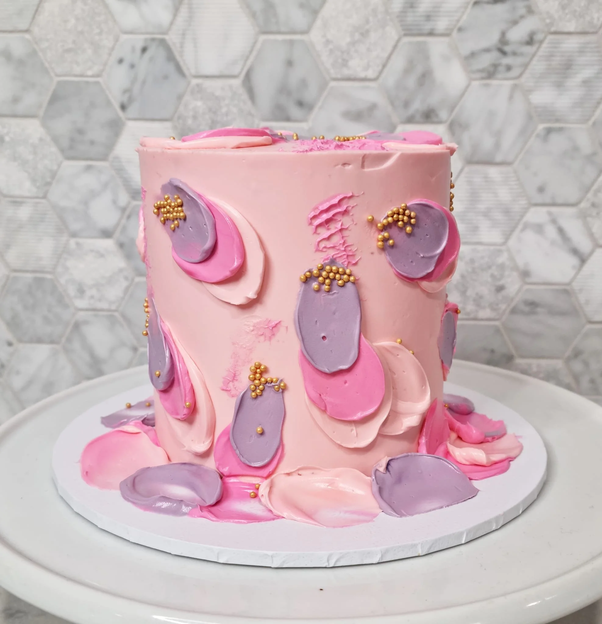 Pink unicorn-themed cake decorated with purple and pink frosting, gold sprinkles, and fondant ears and horn, on a white cake board.