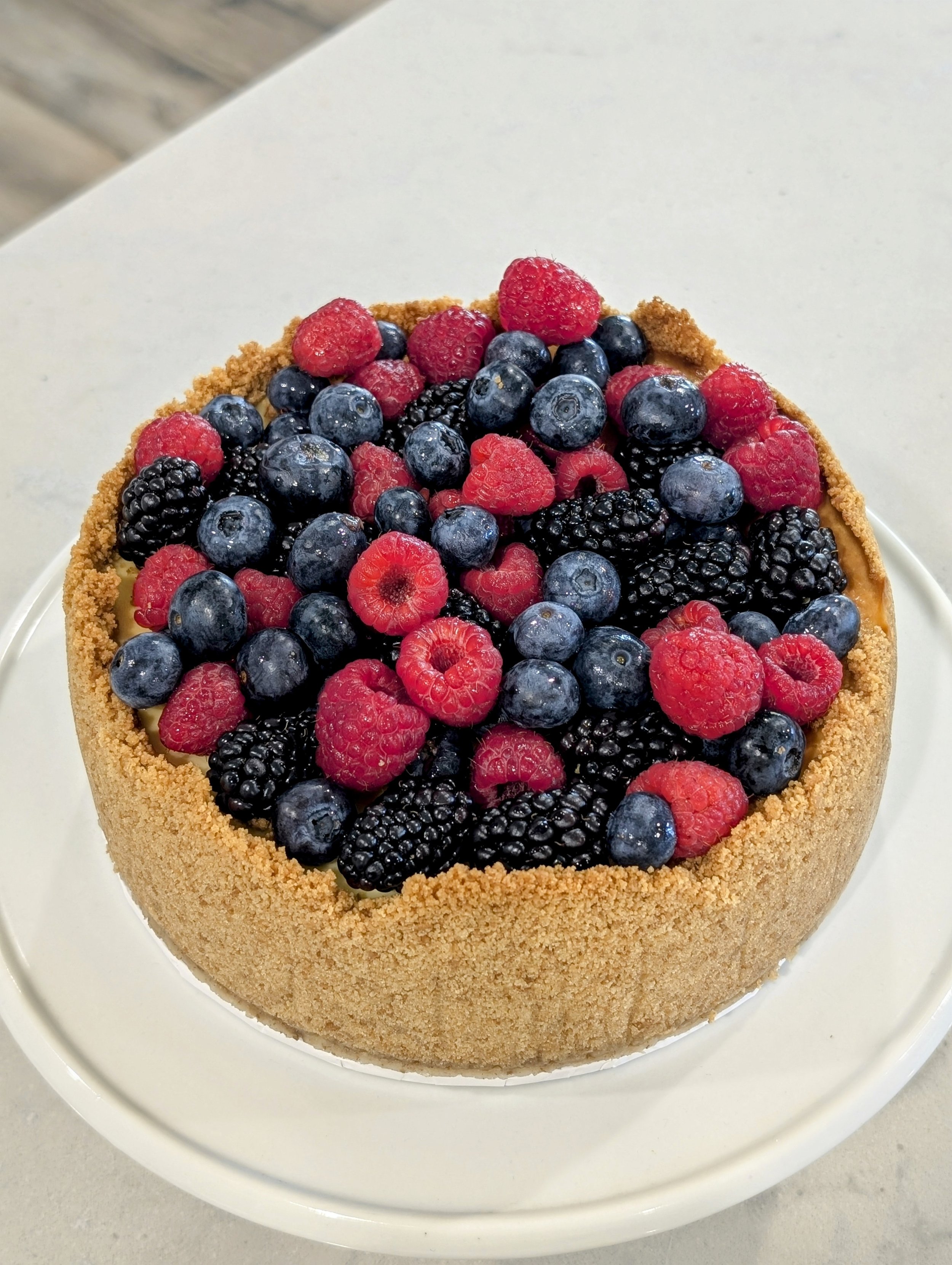 Cake with a graham cracker crust topped with mixed fresh berries including raspberries, blueberries, and blackberries
