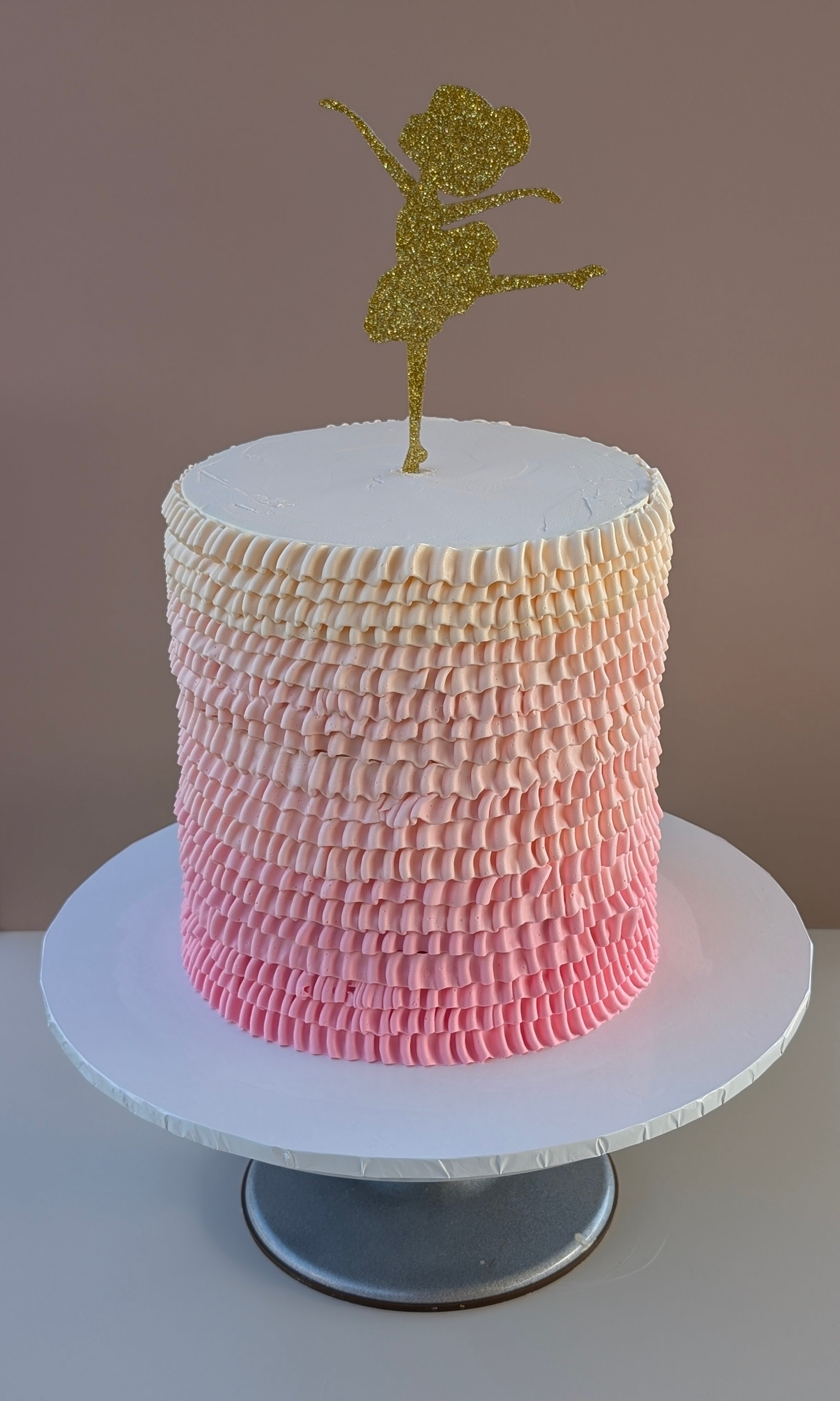 A tiered cake with ruffled pink and white icing and a glittery gold fairy silhouette cake topper.