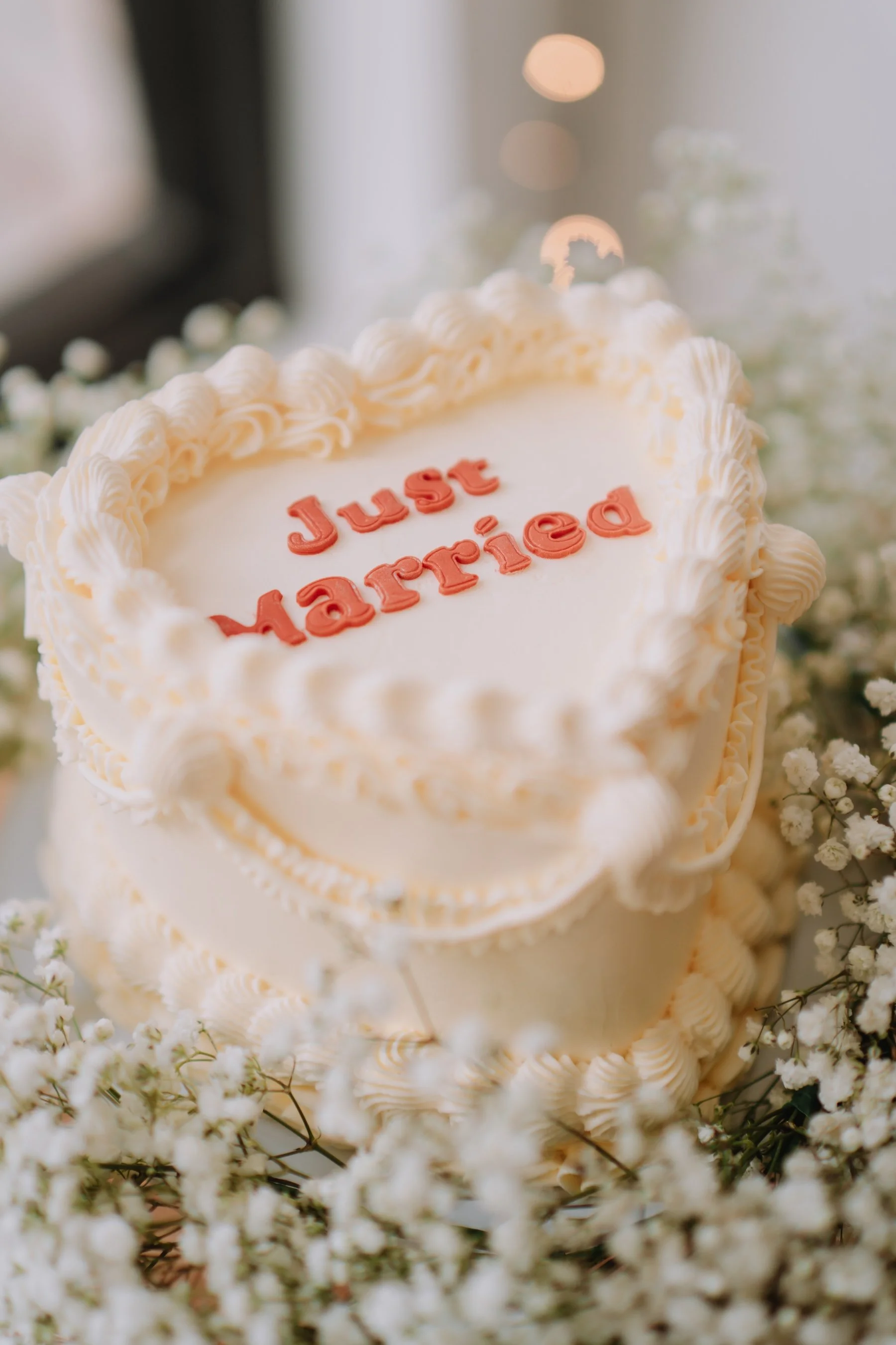 Heart-shaped wedding cake with white frosting and decorative piping, surrounded by white flowers, with the words "Just Married" written in red on top.