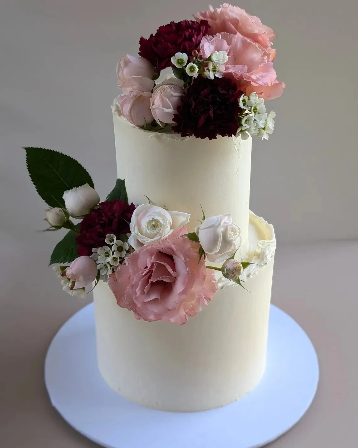 Two-tiered wedding cake decorated with pink and white flowers, including roses and blooms, with green leaves.