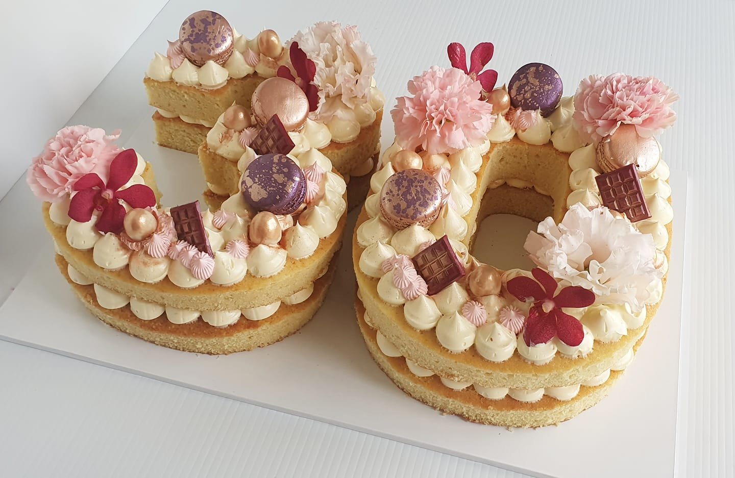 A cake shaped like the number 10 decorated with pink and purple flowers, macarons, and chocolate pieces.