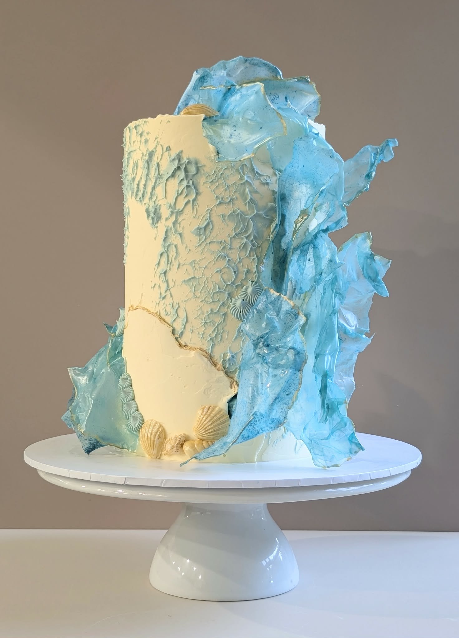 An artistic cake decorated with blue and white abstract ocean-inspired elements, including seashells.