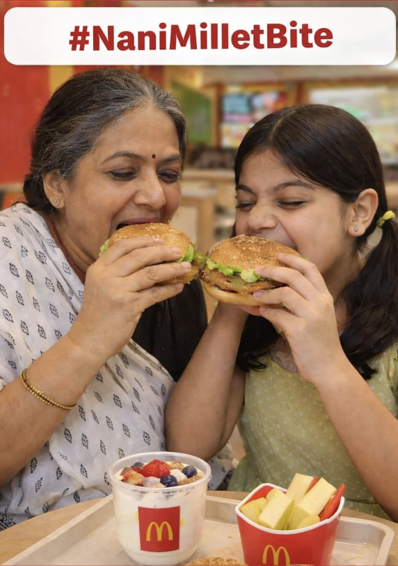 A woman and girl sharing burgers at McDonald's, with yogurt and apple slices on the tray. The caption reads #NaniMilletBite.