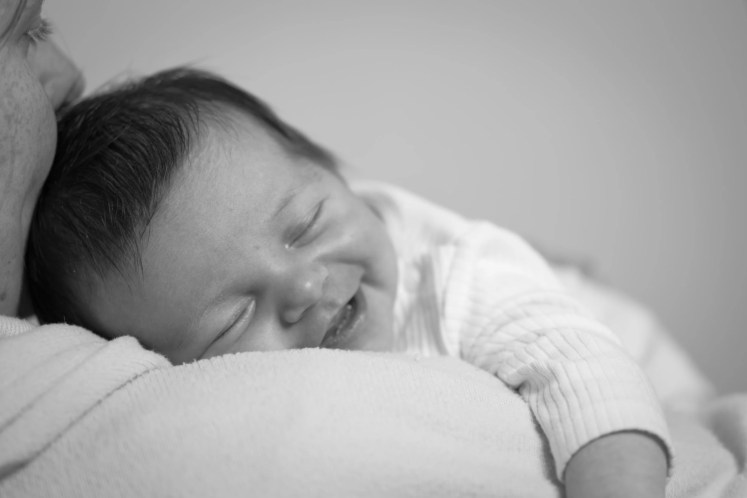 Black and white photo of a young child smiling peacefully while resting on an adult's shoulder, with the child's eyes closed and hair slightly damp.