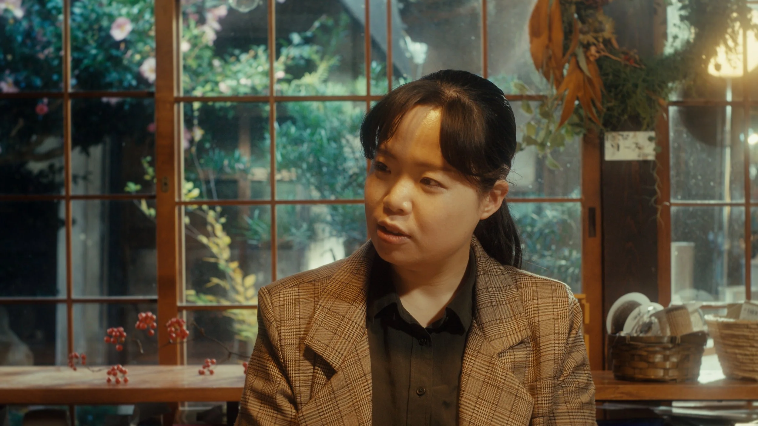 木製の窓の向こうに庭の風景と女性が映っている