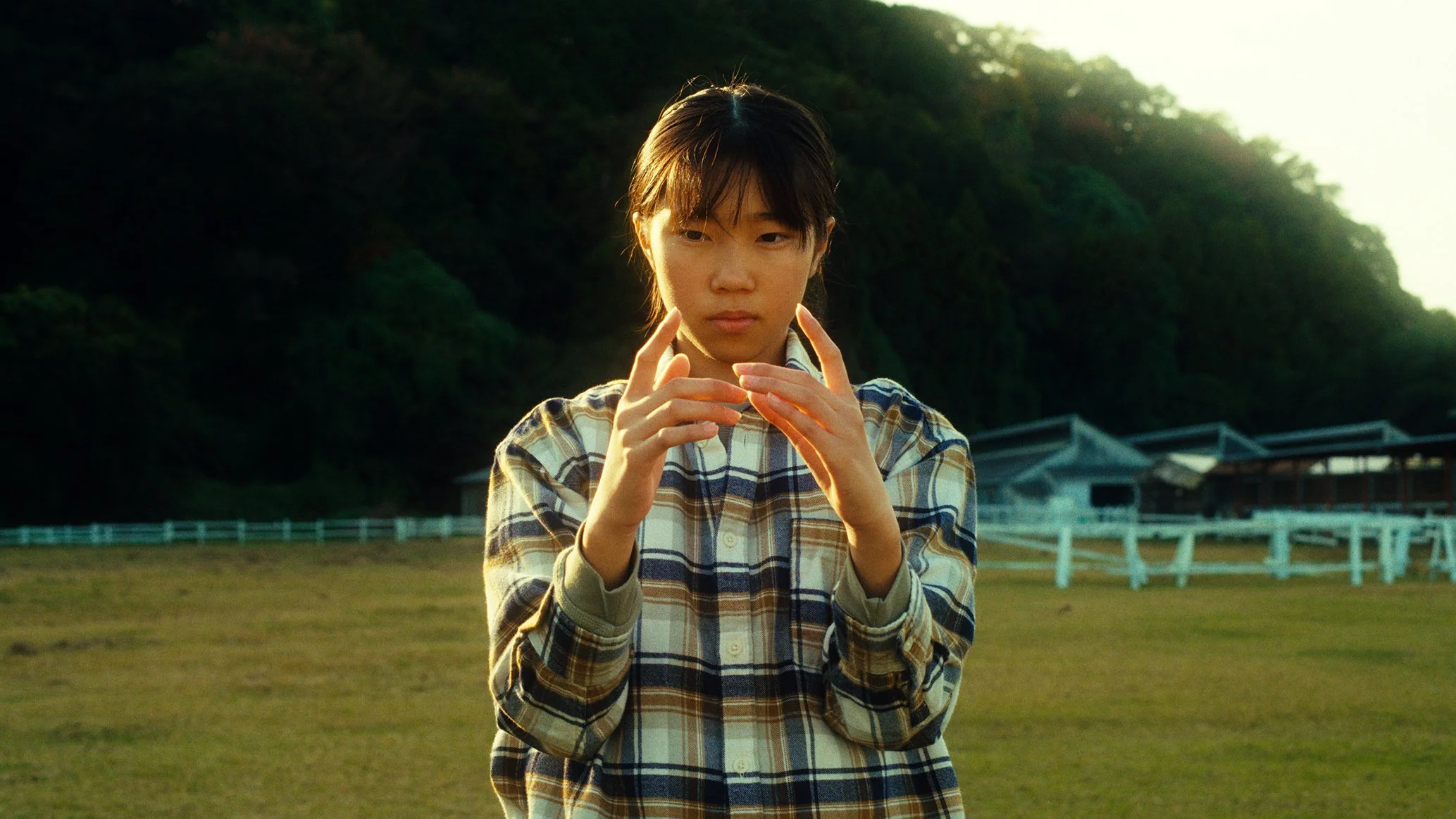 チェック柄のシャツを着た若い女性が外の広い草原で手を動かしている