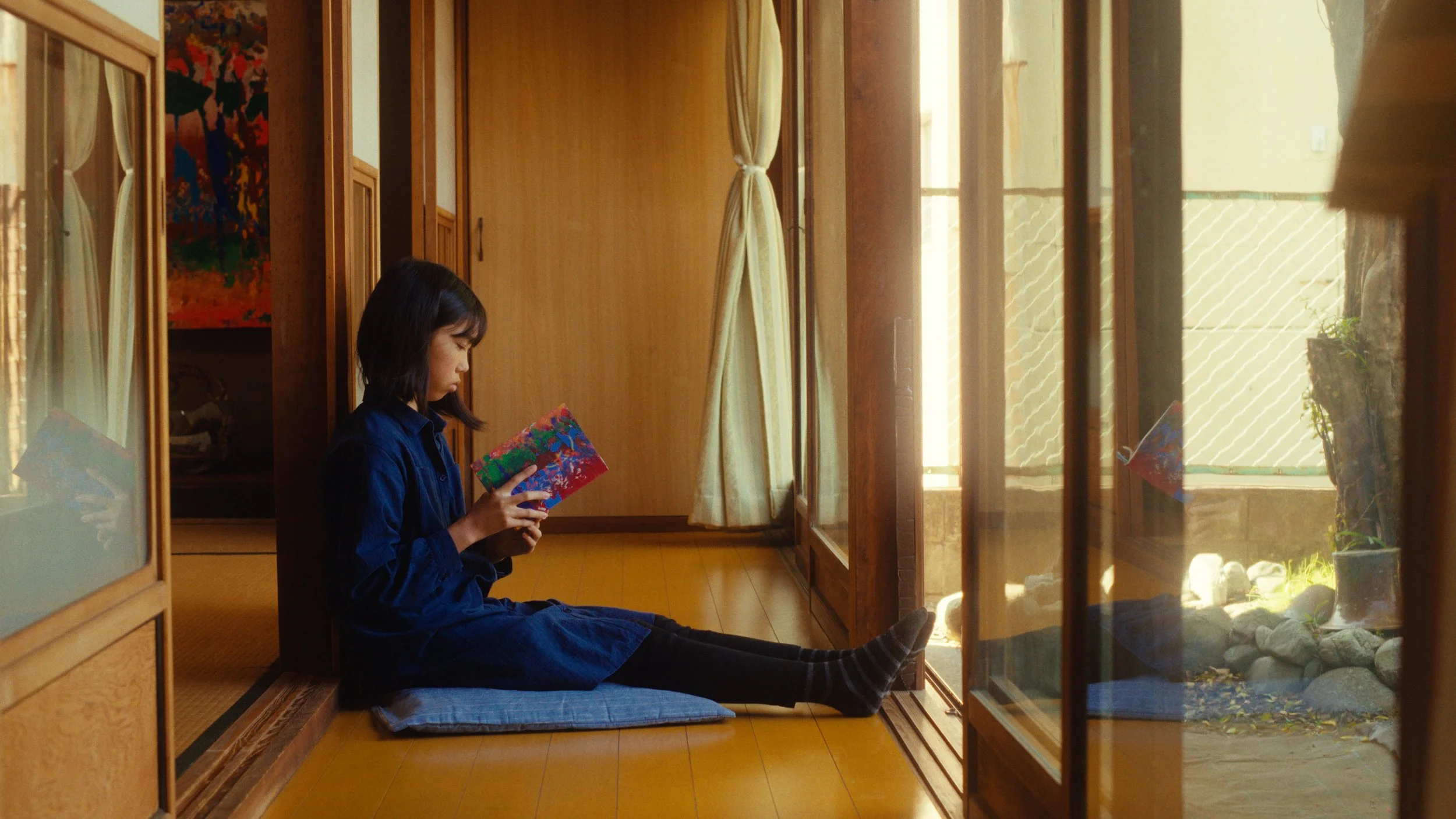 座敷に座って外を見ながら本を読んでいる女性