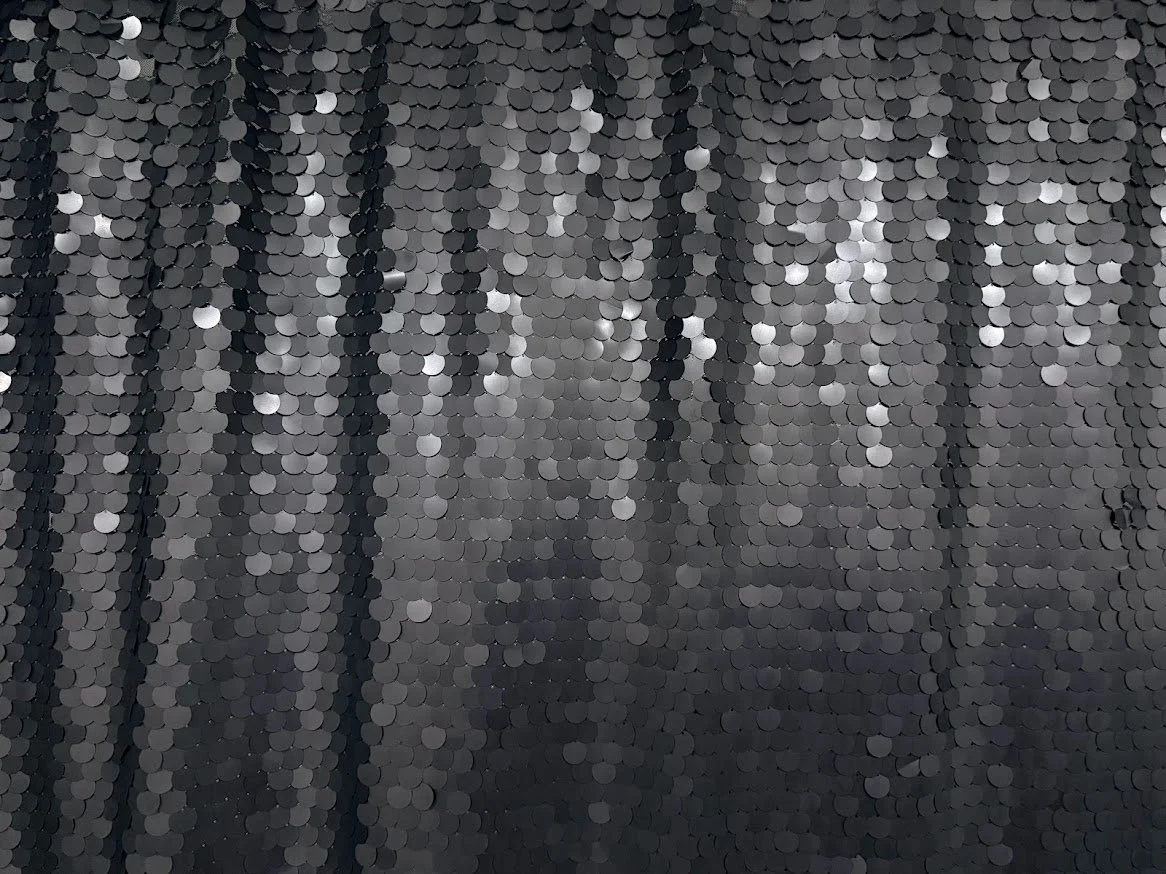 Close-up of a sequined fabric with black and silver sequins arranged in vertical stripes.