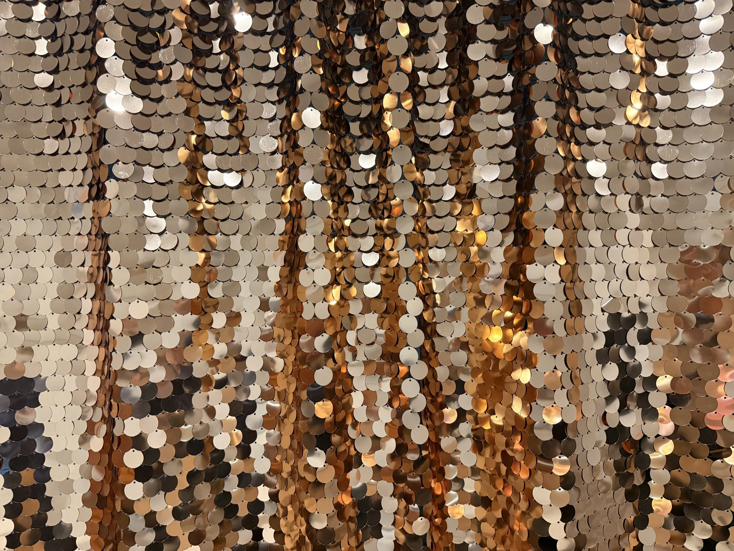 A wall decorated with golden, silver, and black sequins that create a shimmering, textured surface.