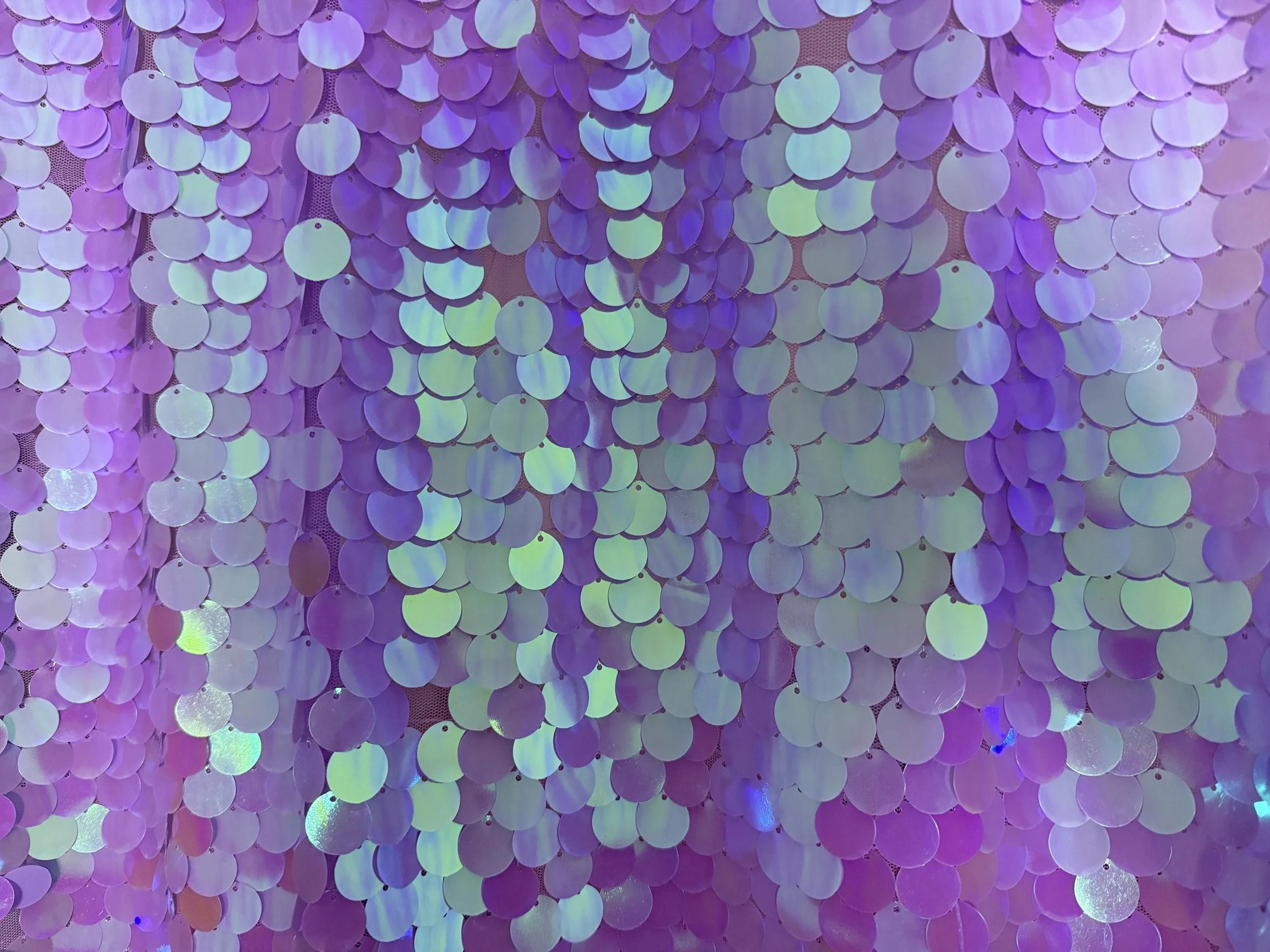 A wall decorated with iridescent purple sequins that reflect light and create a shimmering, colorful effect.