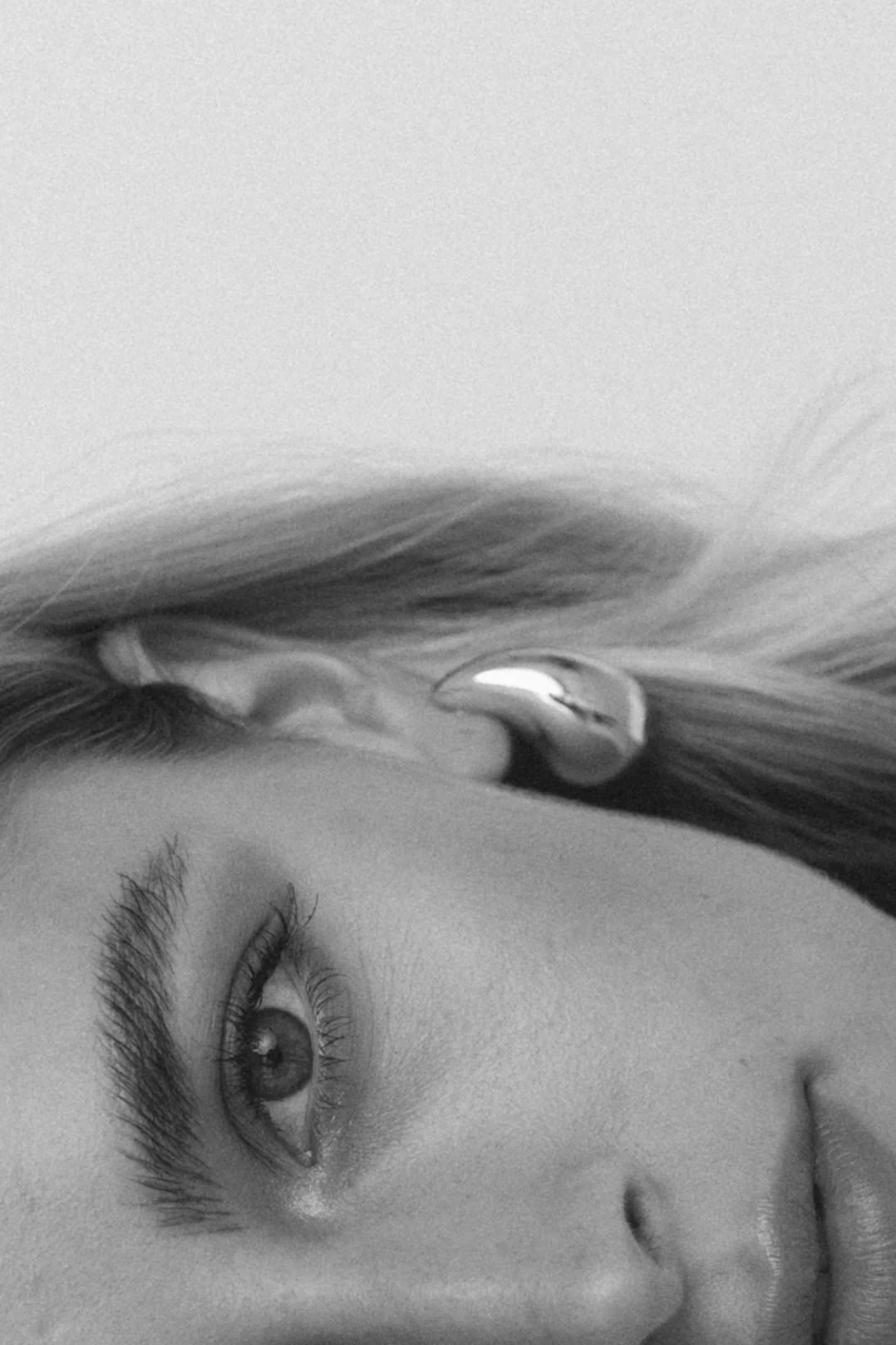 Eine Nahaufnahme eines menschlichen Gesichts mit Fokus auf das linke Auge, das sehr detailliert ist, in Schwarz-Weiß, neben einem Ohr mit einem Ohrstecker.