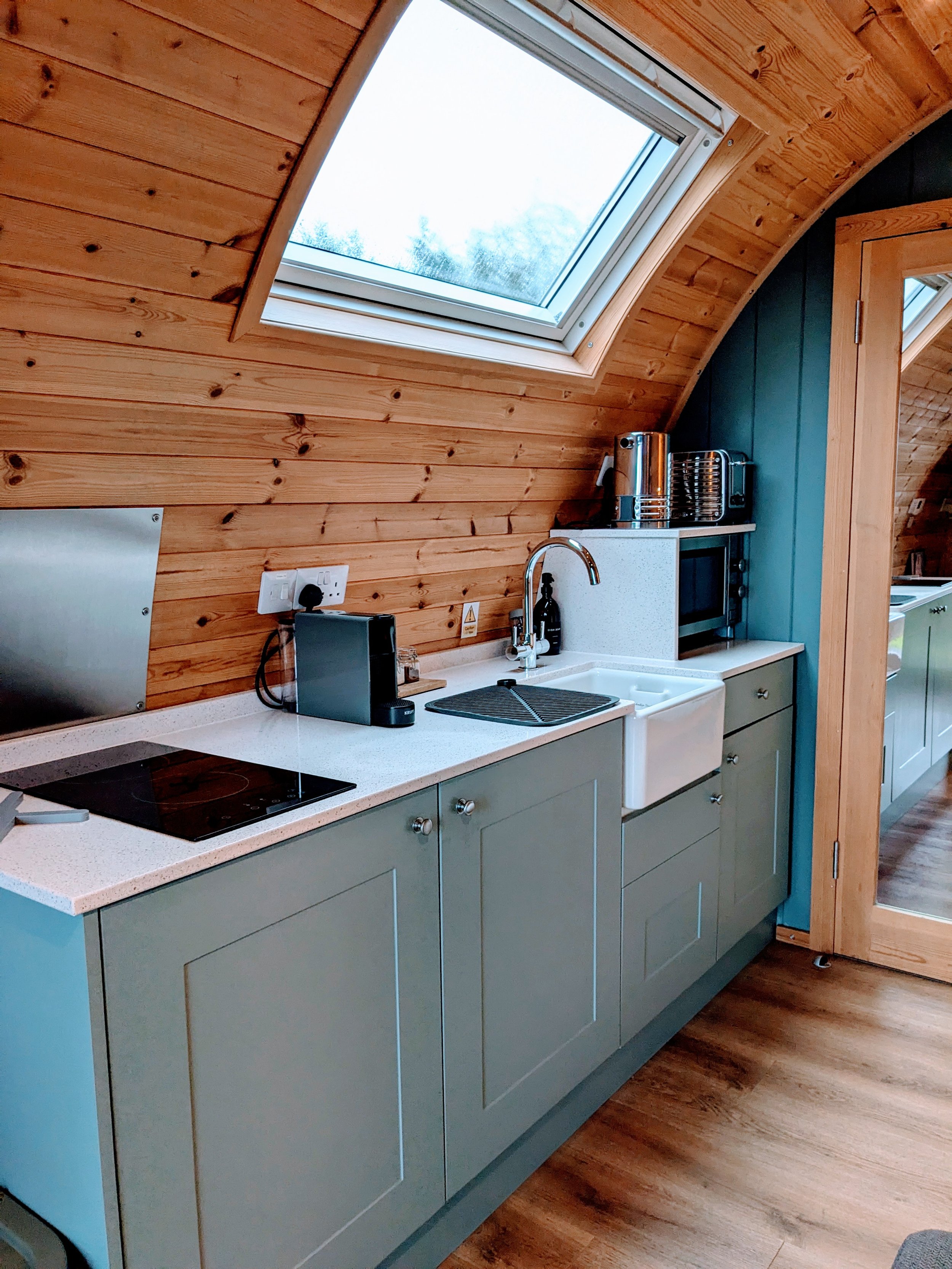 Kitchen with light blue cabinets, a white farmhouse sink, a black electric stove, and a wooden ceiling with a skylight window.