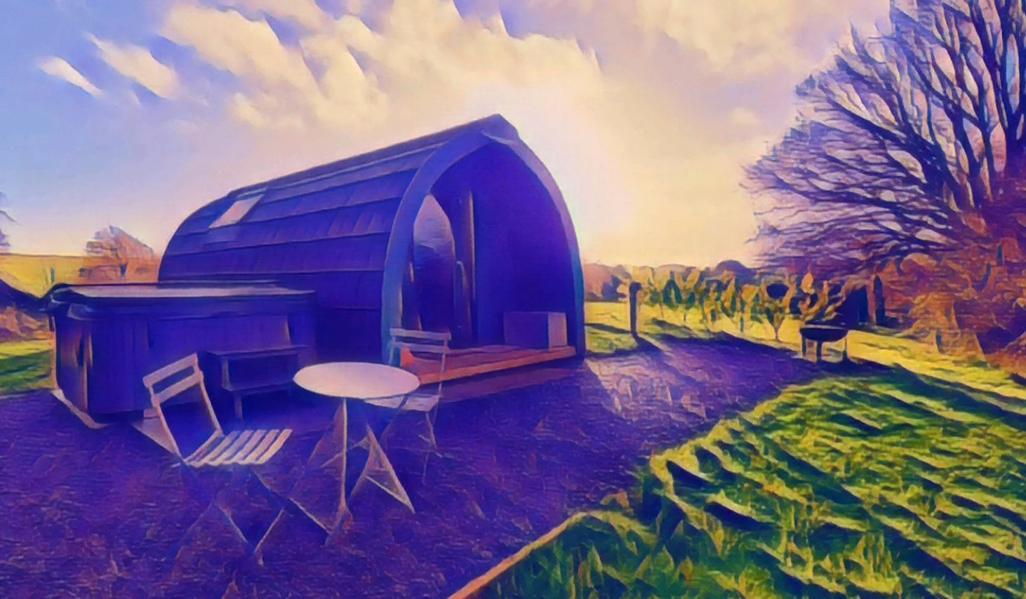 A Glamping Pod, set on a working farm on a grassy field, with two chairs and a round table in the foreground, a private hot tub a firepit on the right, and trees in the background under a partly cloudy sky.