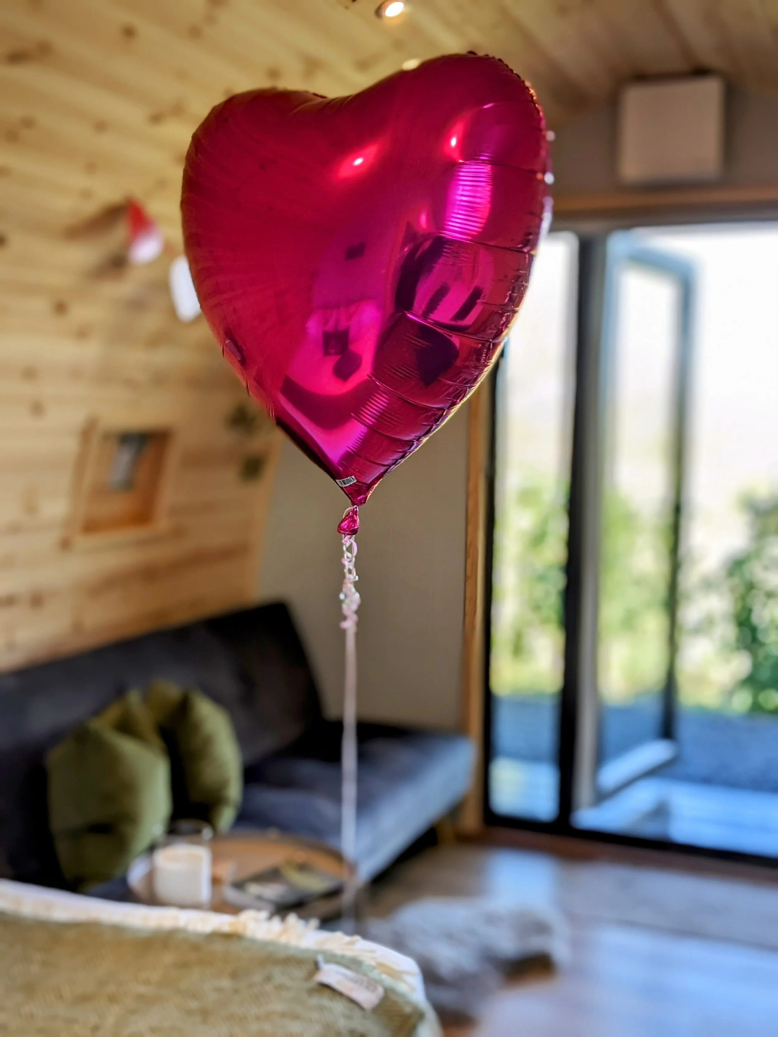 Pink heart-shaped helium balloon floating indoors with a blurred background of a cozy living room.