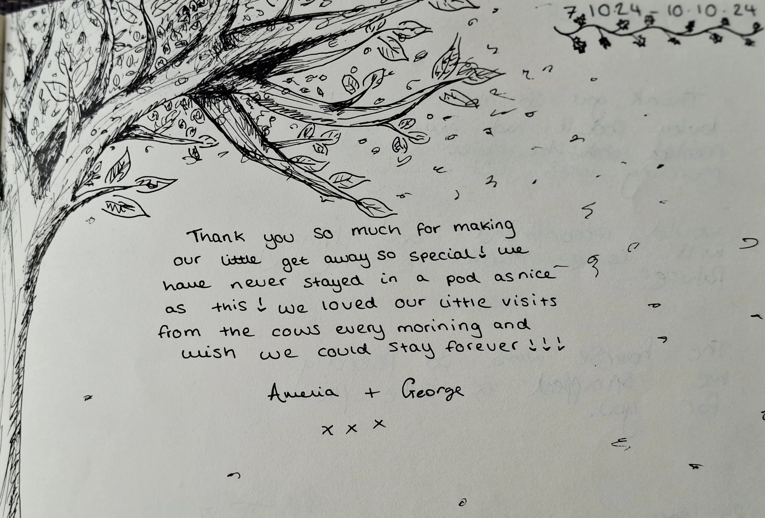 A handwritten thank you note on a white card with a sketch of a tree in the top left corner. The note expresses gratitude for making a special getaway, mentions enjoying visits from cows, and wishes to stay forever. It is signed by Amelia and George.