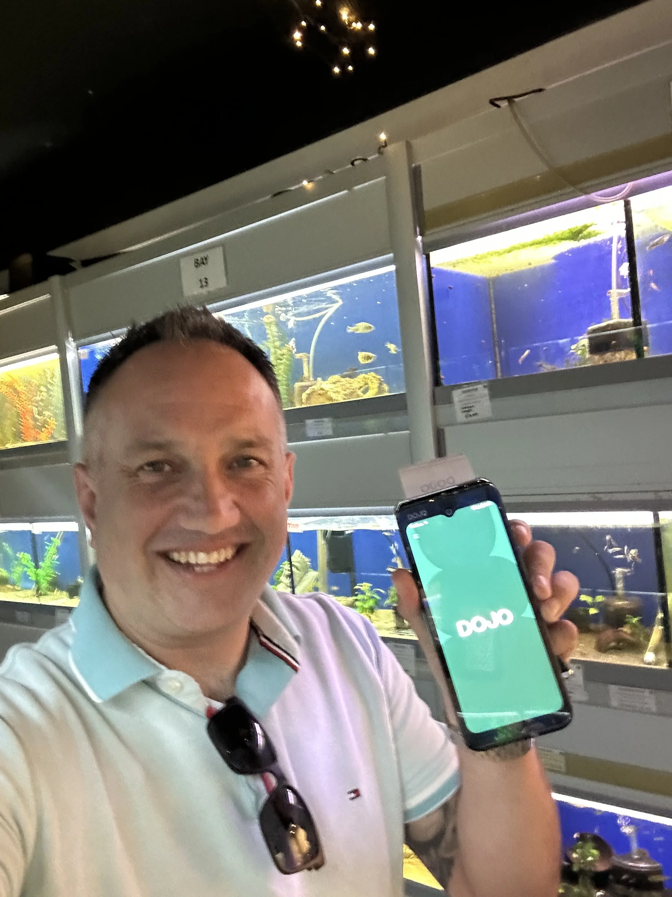 Ben Buey holding a Dojo Go MAX  in front of various fish tanks in an aquarium or pet store.