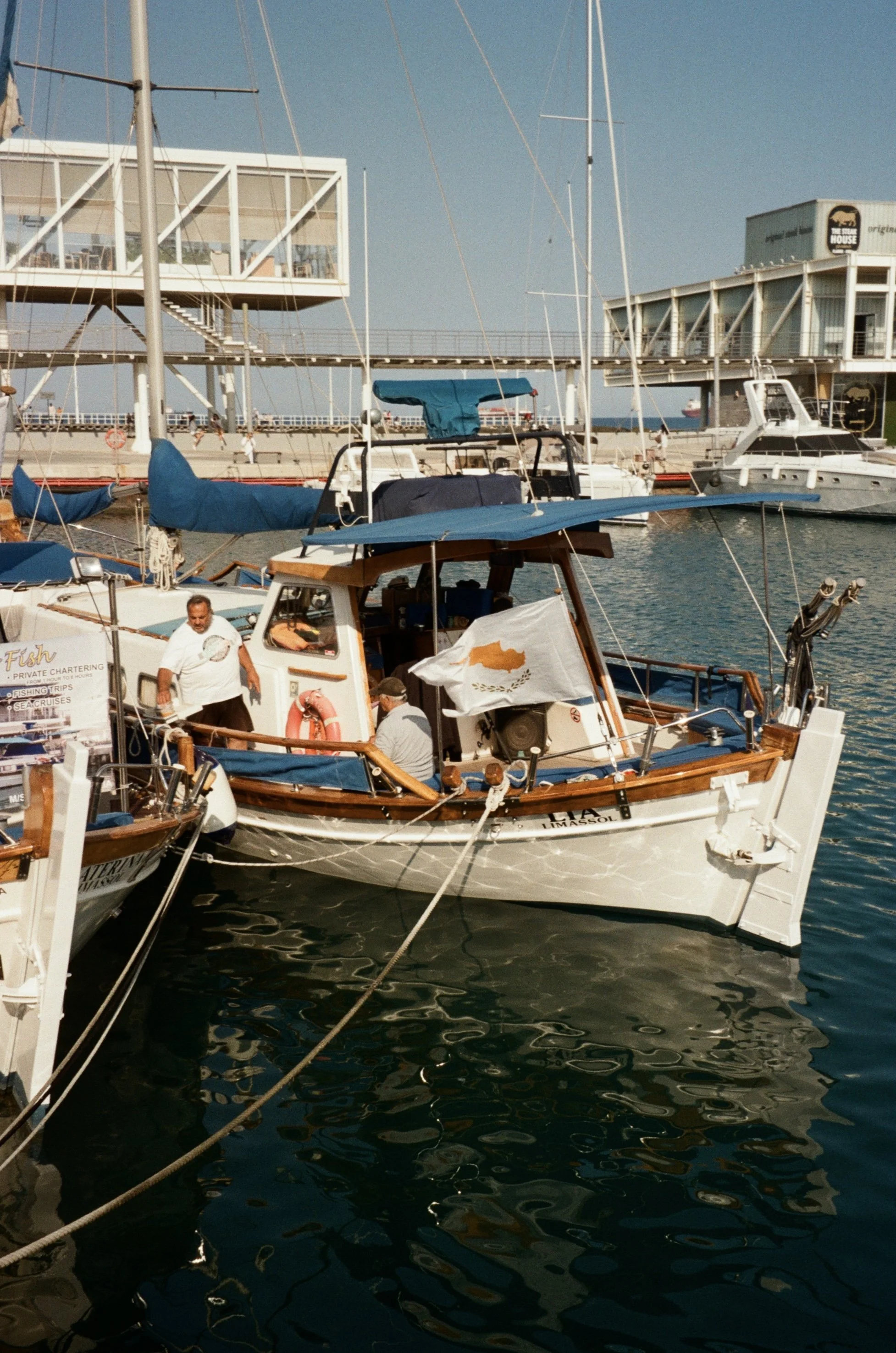 Boats docked at a marina with a building in the background, under a clear blue sky.