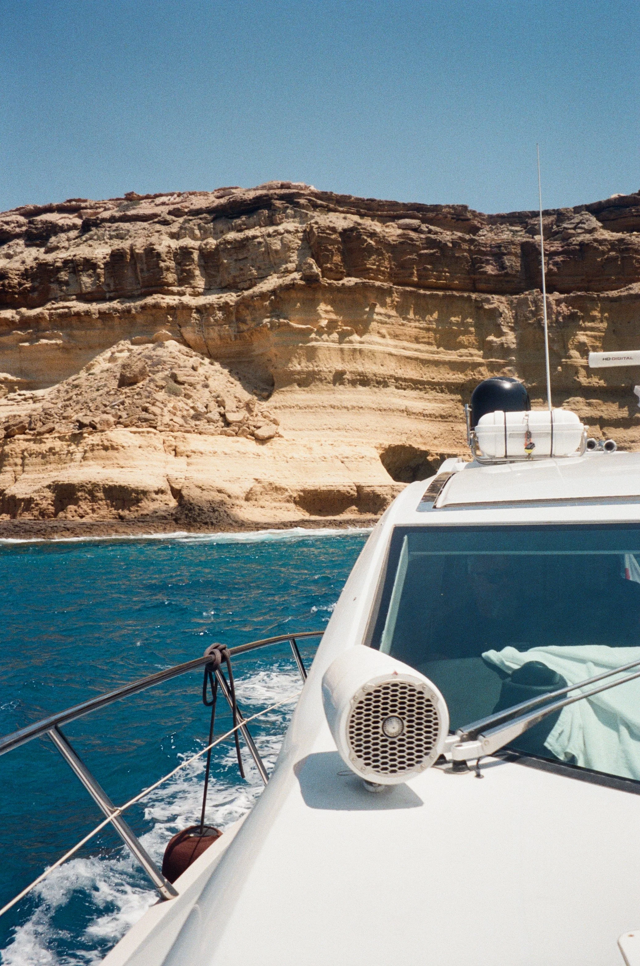 View from a boat showing a rocky coastline and clear blue water under a bright sky.