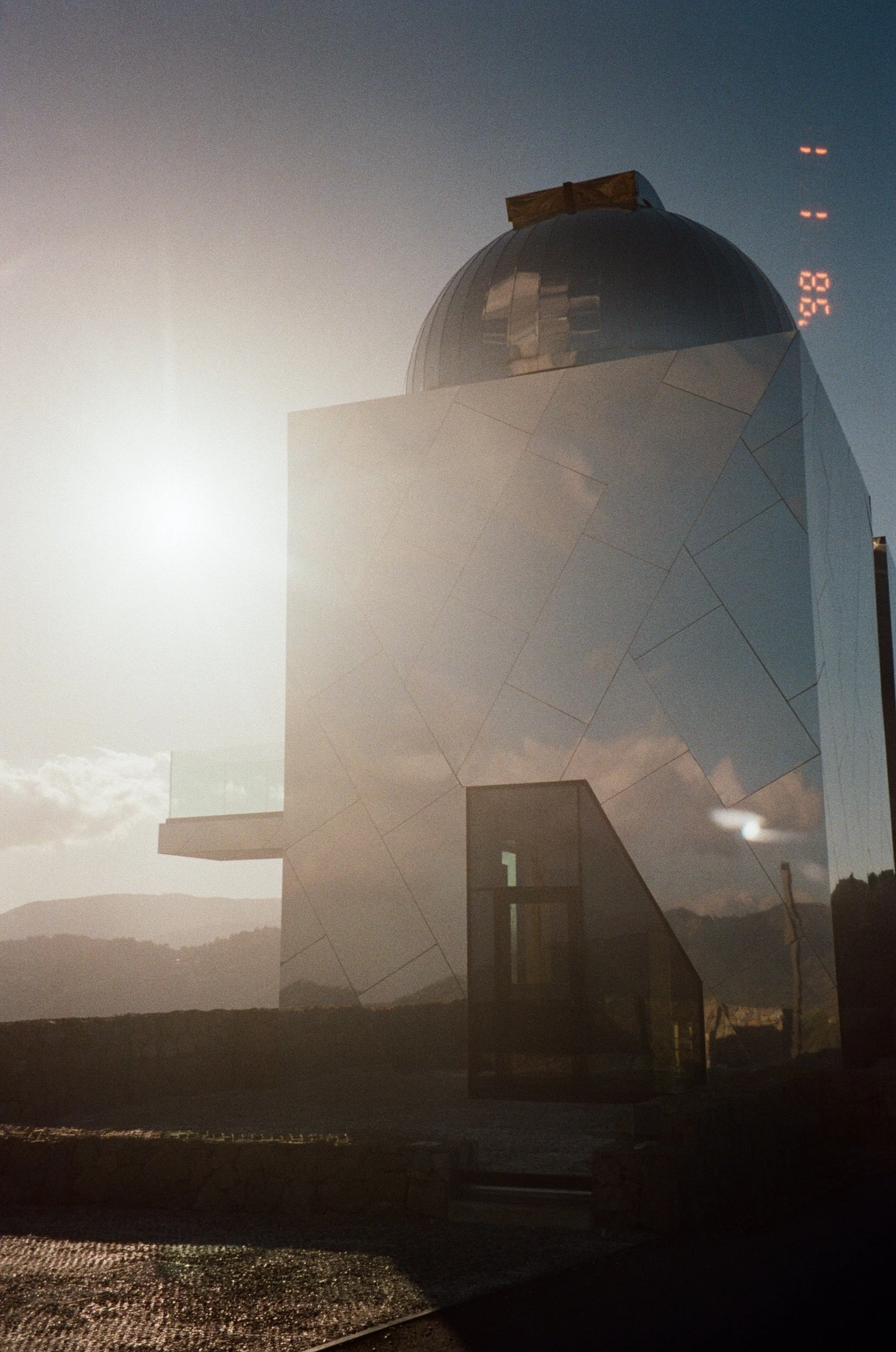 Modern building with reflective metallic facade and a dome at the top, set against a bright sky with mountains in the background.